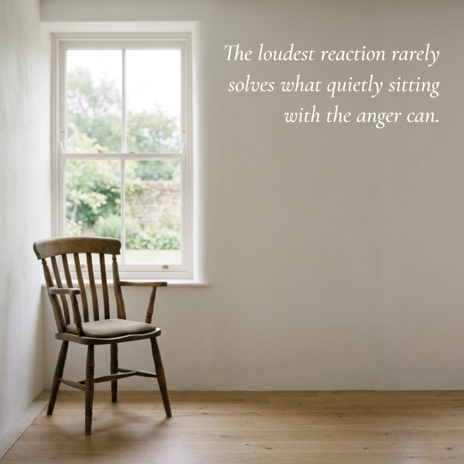 Minimalist photo of a wooden chair by a bright window. The large white wall to the right displays the quote, 'The loudest reaction rarely solves what quietly sitting with the anger can.'