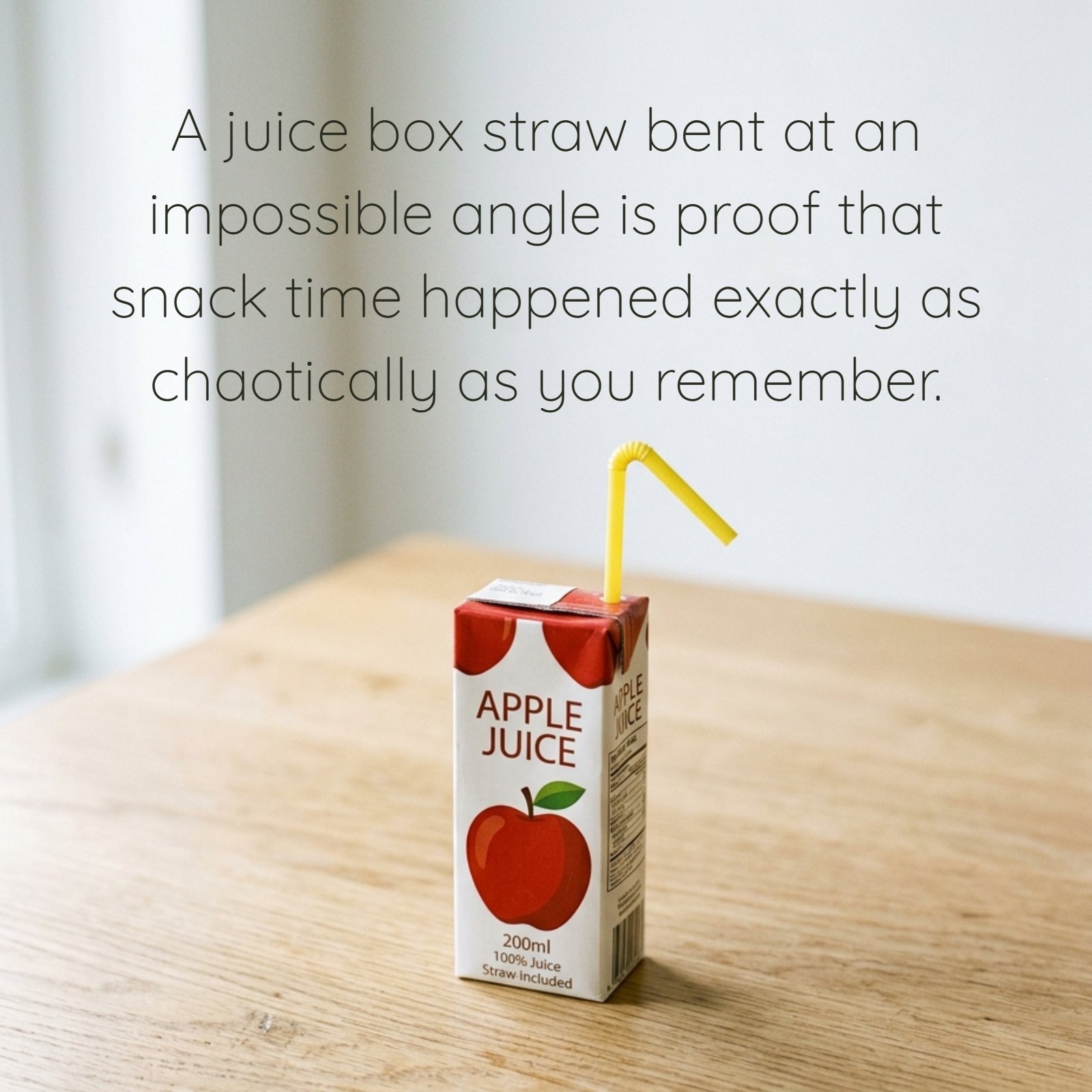 Minimalist photo of a single apple juice carton on a wooden table with a sharply bent yellow straw. The image includes the text 'A juice box straw bent at an impossible angle is proof that snack time happened exactly as chaotically as you remember.'