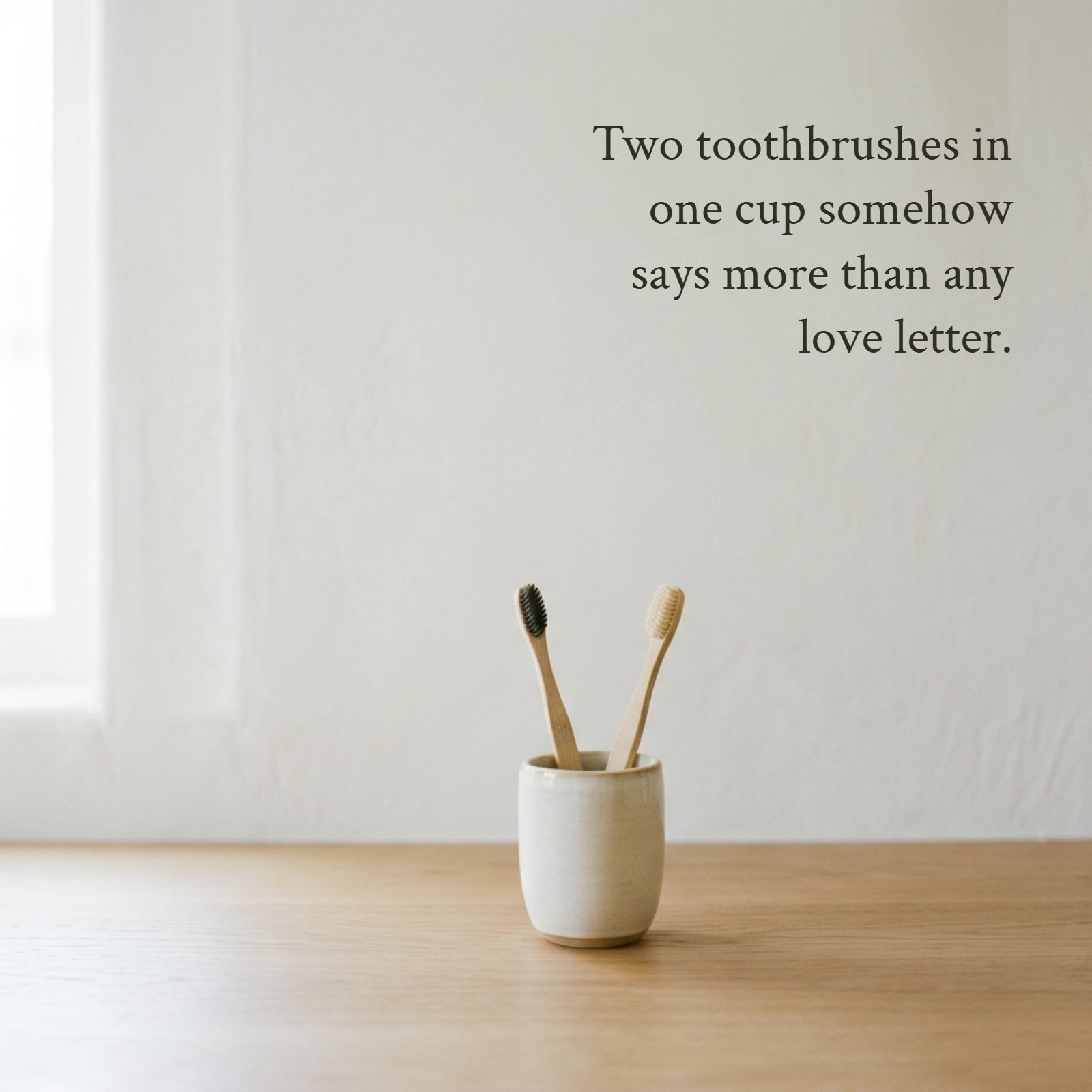 Minimalist bathroom counter image with text that reads: Two toothbrushes in one cup somehow says more than any love letter.