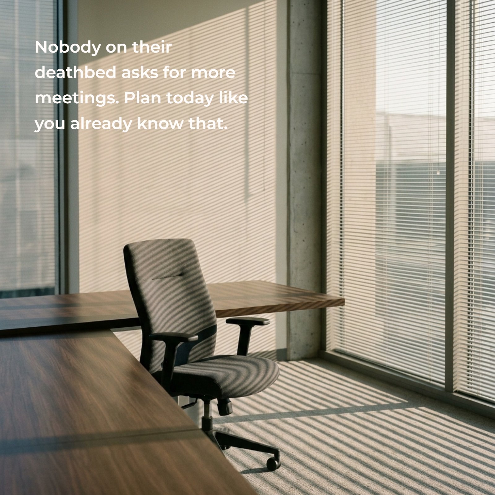 Minimalist image of an empty modern office chair facing a corner desk, with strong horizontal shadows from window blinds.