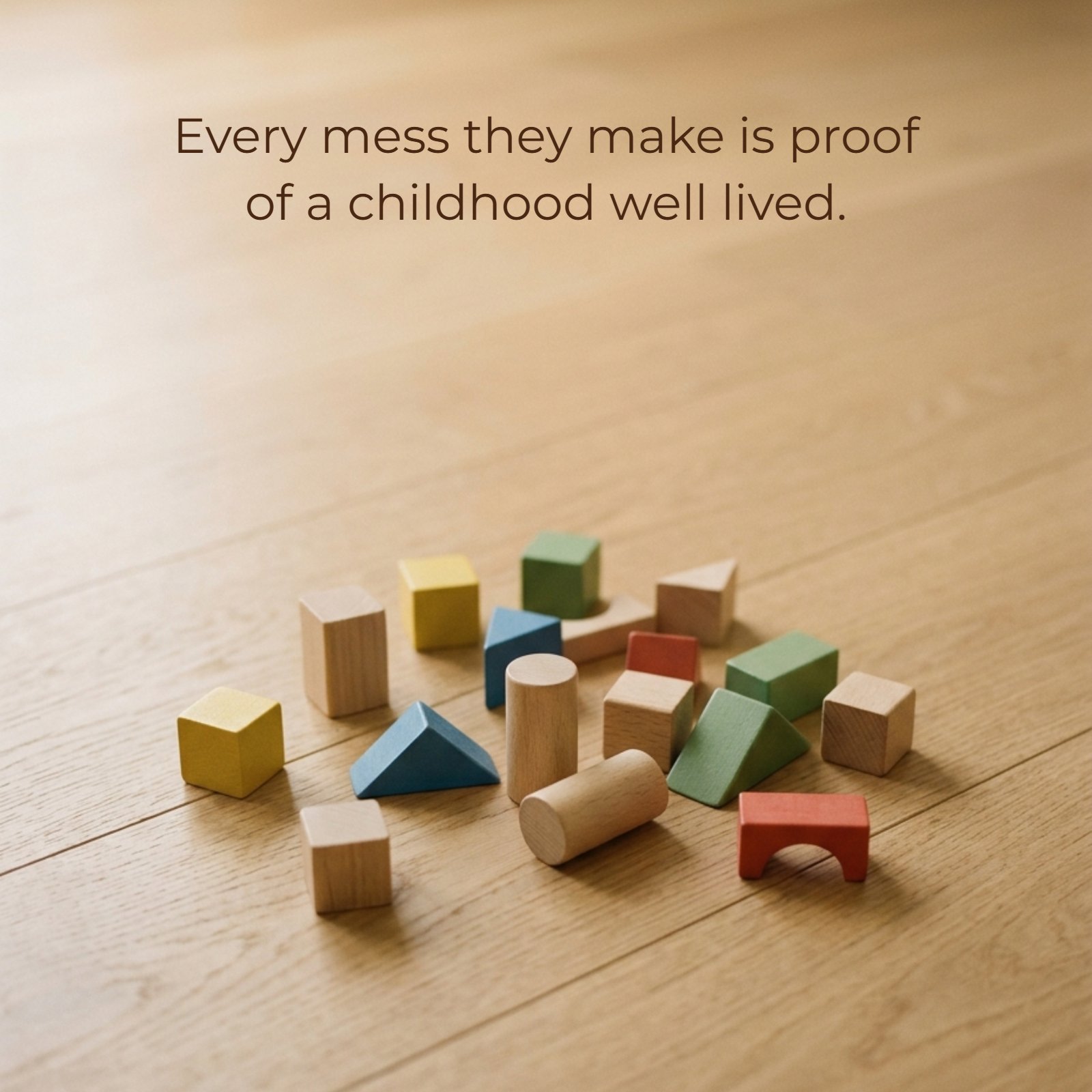 A minimalist vertical photograph of scattered colorful wooden building blocks on a plain wooden floor with the quote text "Every mess they make is proof of a childhood well lived" in light font in the negative space above.