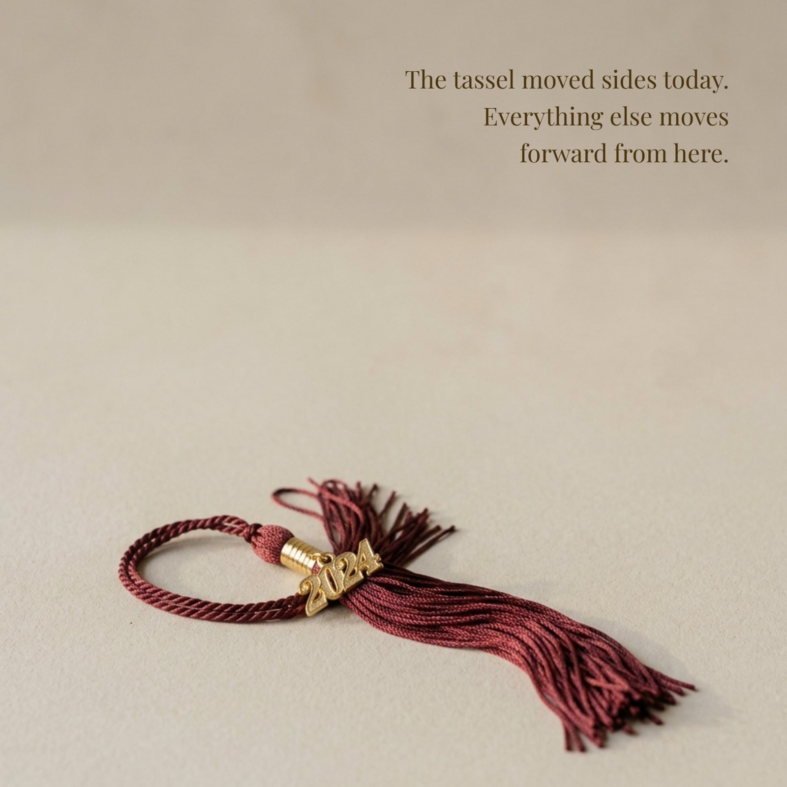 A maroon graduation tassel rests on a plain surface with the quote 'The tassel moved sides today. Everything else moves forward from here.' written nearby.