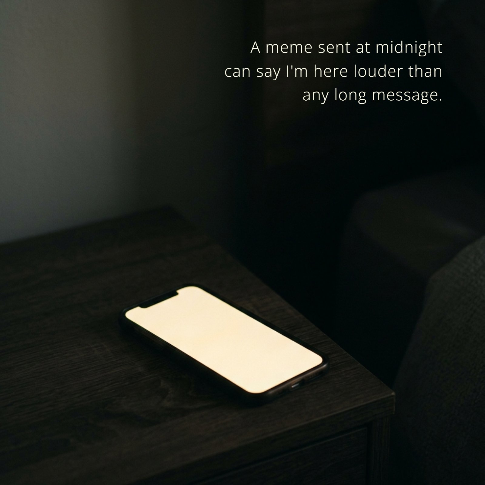 A minimalist photo of a smartphone lying face up on a dark wooden nightstand. The screen is glowing with a warm, soft, yellowish-white light in a dim, shadowed room. Overlaid on the screen is the quote text: "A meme sent at midnight can say I'm here louder than any long message."