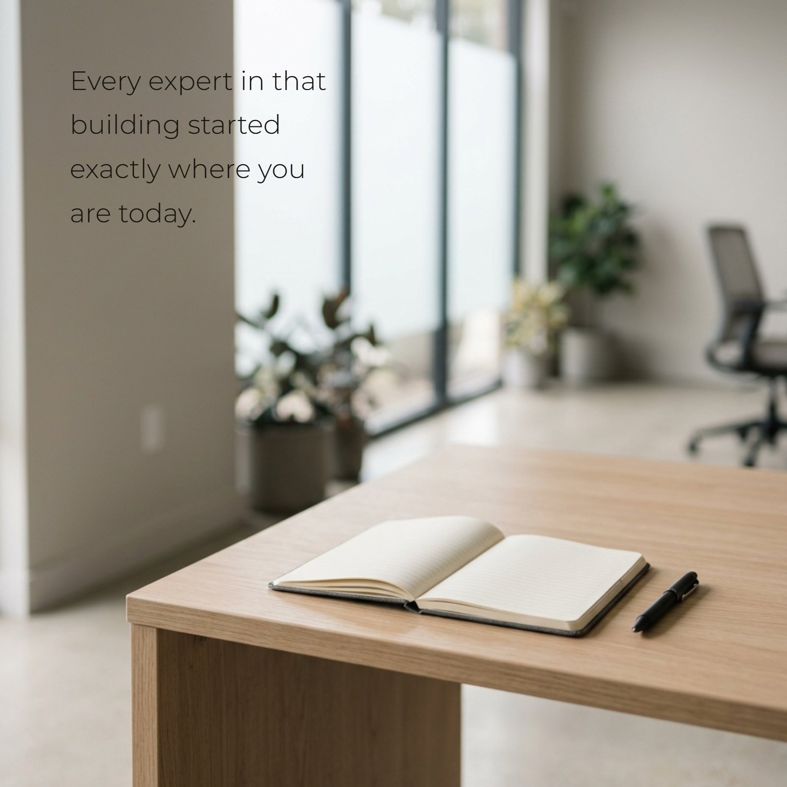 Minimalist photo of an open notebook and pen on a wooden desk with blurred background and a powerful text overlay: Every expert in that building started exactly where you are today.