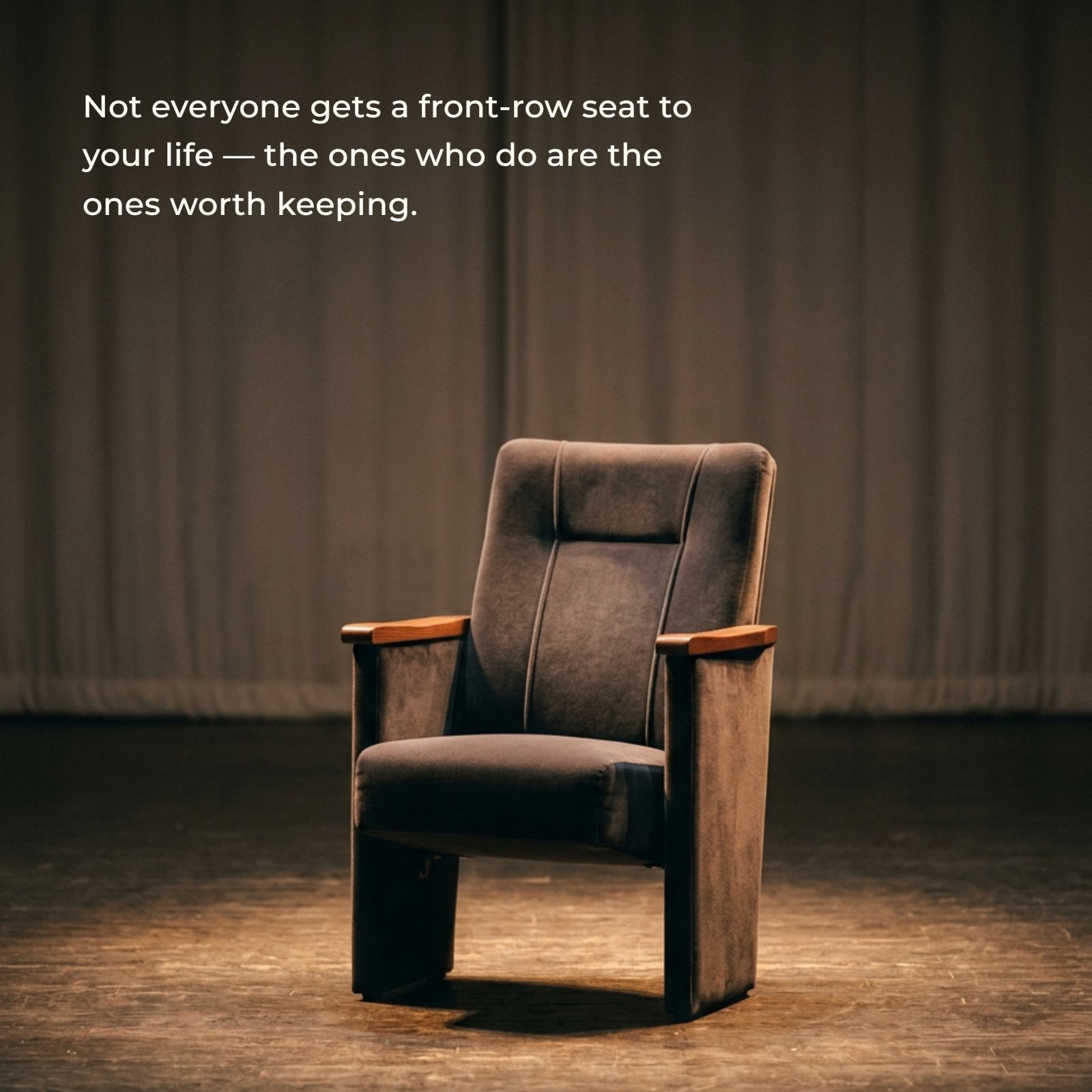Minimalist image of a solitary grey plush theater chair on a wooden stage, illuminated by a warm spotlight from above against a draped background. This image is meant for overlaying the text, "Not everyone gets a front-row seat to your life — the ones who do are the ones worth keeping."