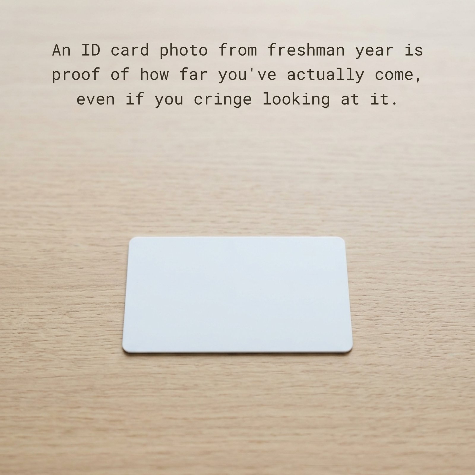 Minimalist 1:1 photograph featuring a single, blank white plastic card resting on a light wood desk. Overlaid on the image is the white text: An ID card photo from freshman year is proof of how far you've actually come, even if you cringe looking at it.