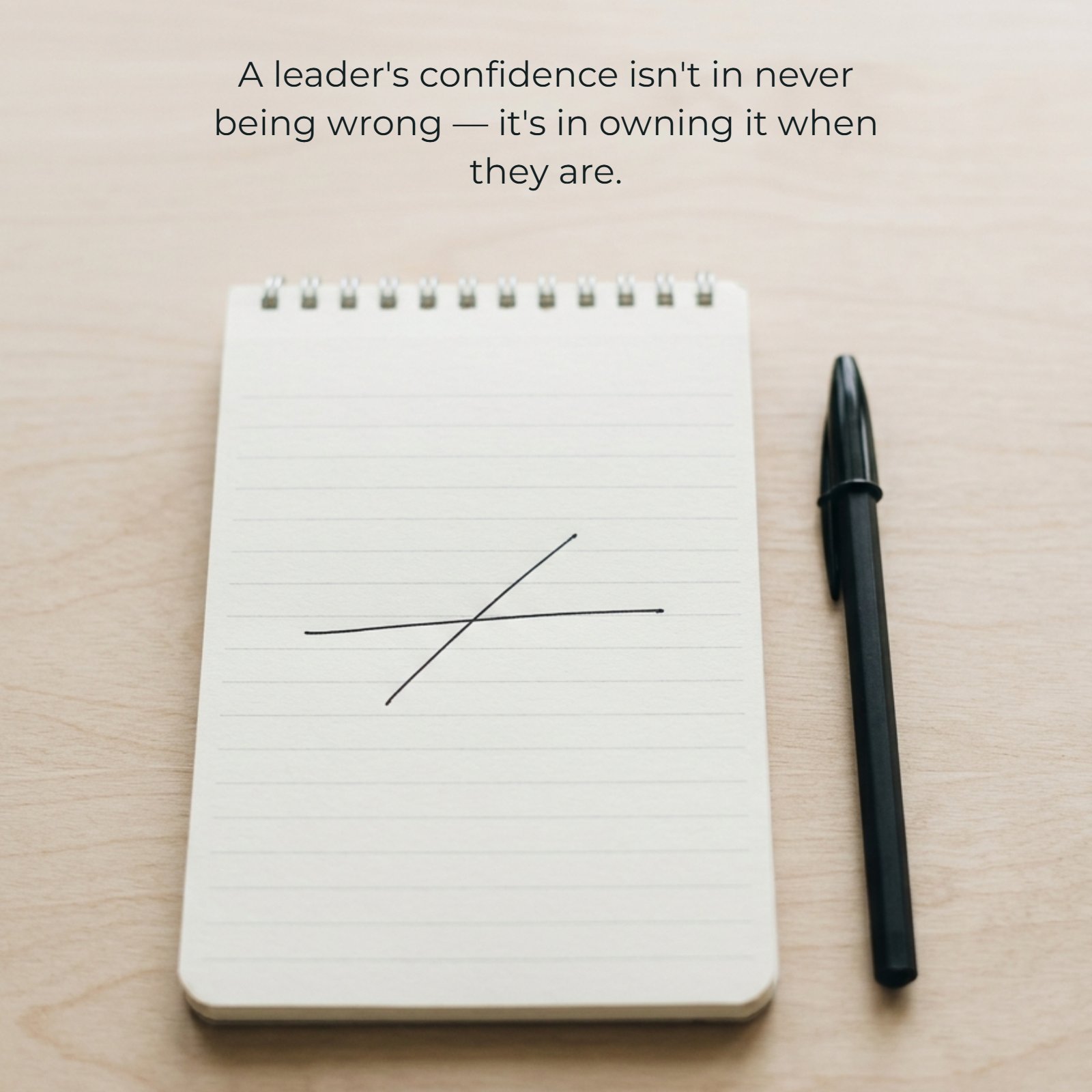 Minimalist 1:1 vertical photo of a lined notepad with a single crossed-out horizontal line, next to a black pen on a light wood surface. Below the line, the text reads: 'A leader's confidence isn't in never being wrong — it's in owning it when they are.'