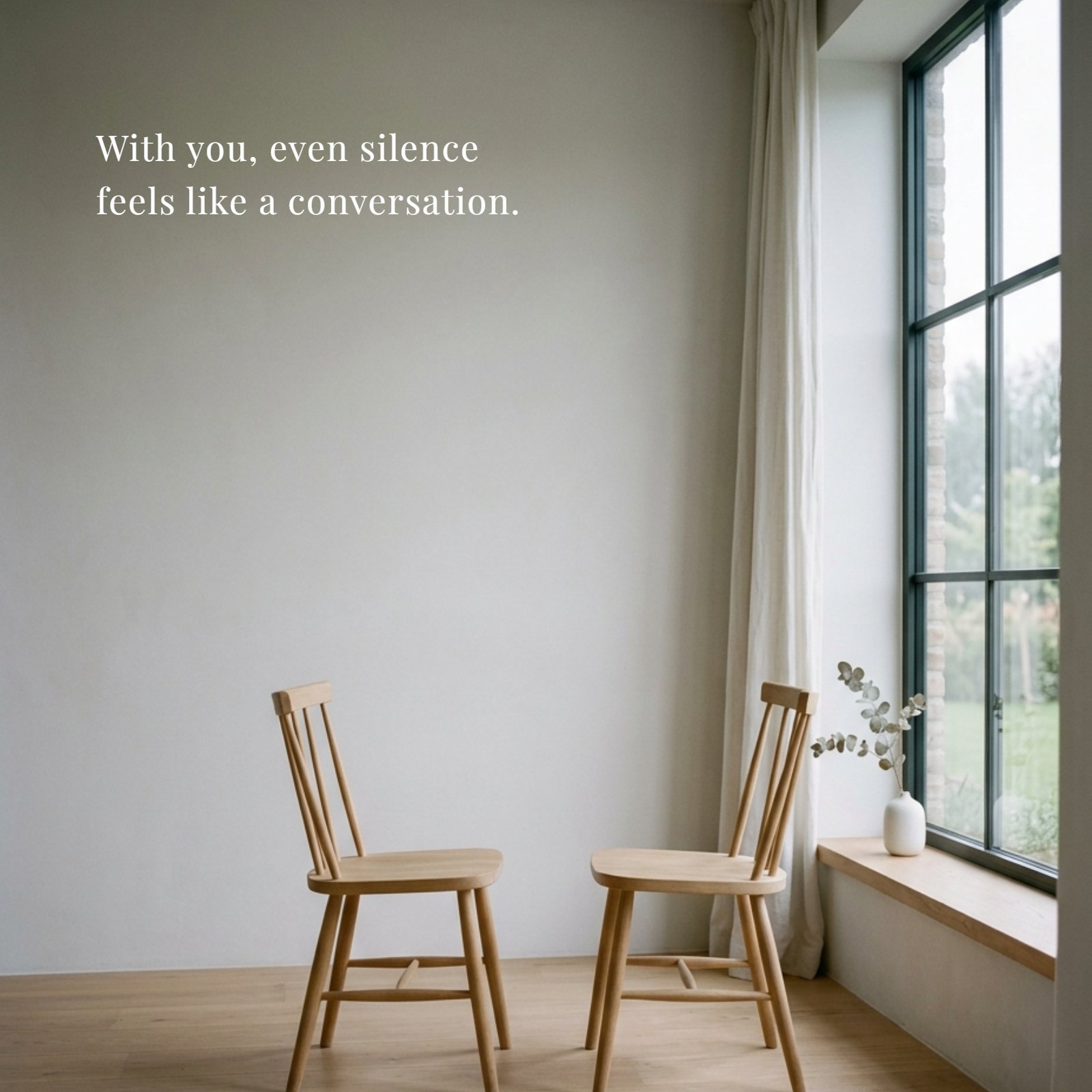 Minimalist 1:1 photograph featuring two simple wooden chairs facing each other beside a large, light-filled window. The abundant negative space is prepared for the overlay of the quote text: "With you, even silence feels like a conversation."