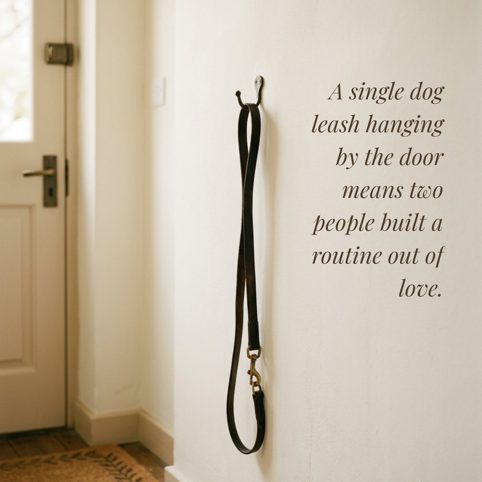 A minimalist photo of a dog leash on a wall hook next to a door, featuring the quote 'A single dog leash hanging by the door means two people built a routine out of love.'