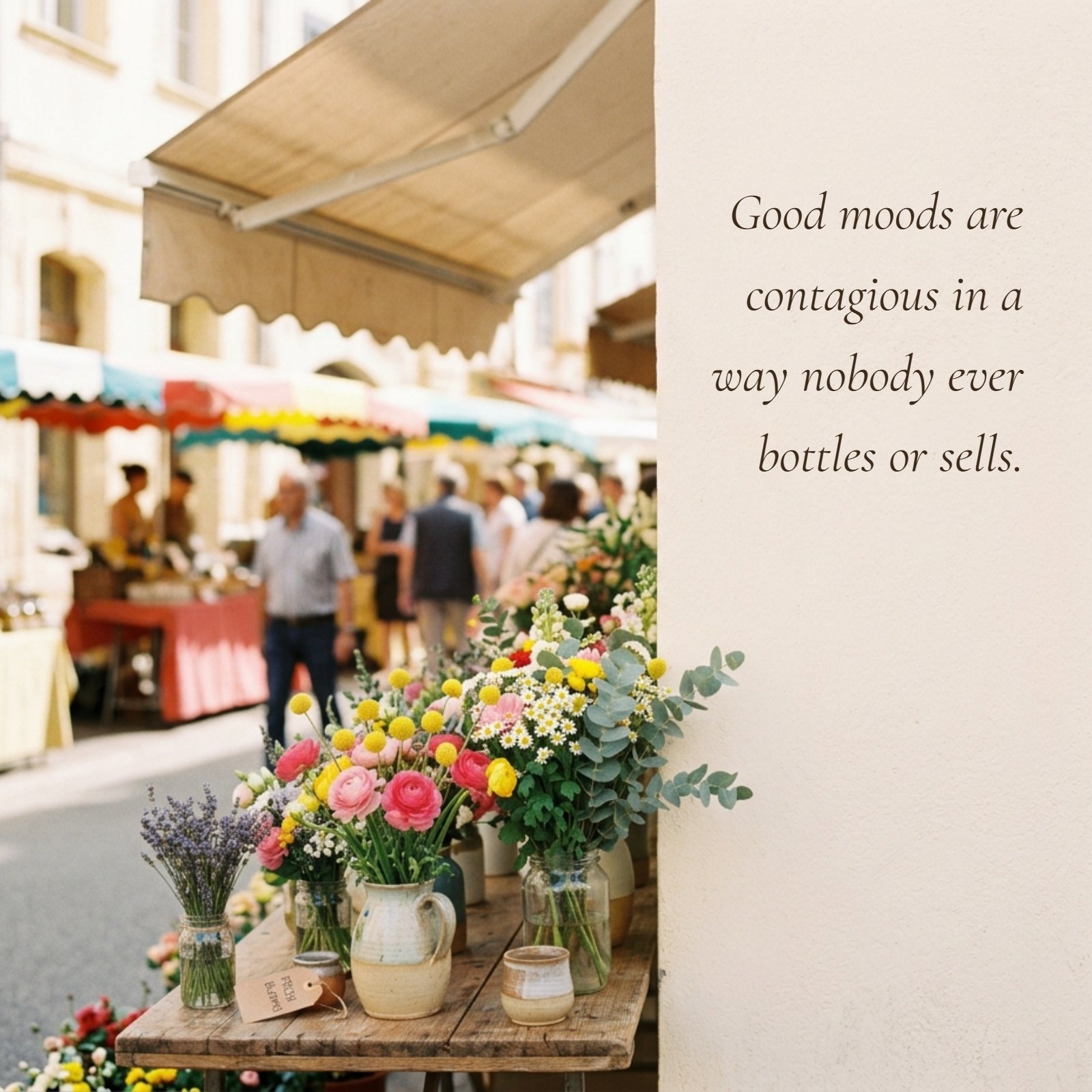 A minimalist photograph shows fresh bouquets of ranunculus and chamomile on a market stall table next to a blank wall containing the quote, "Good moods are contagious in a way nobody ever bottles or sells."