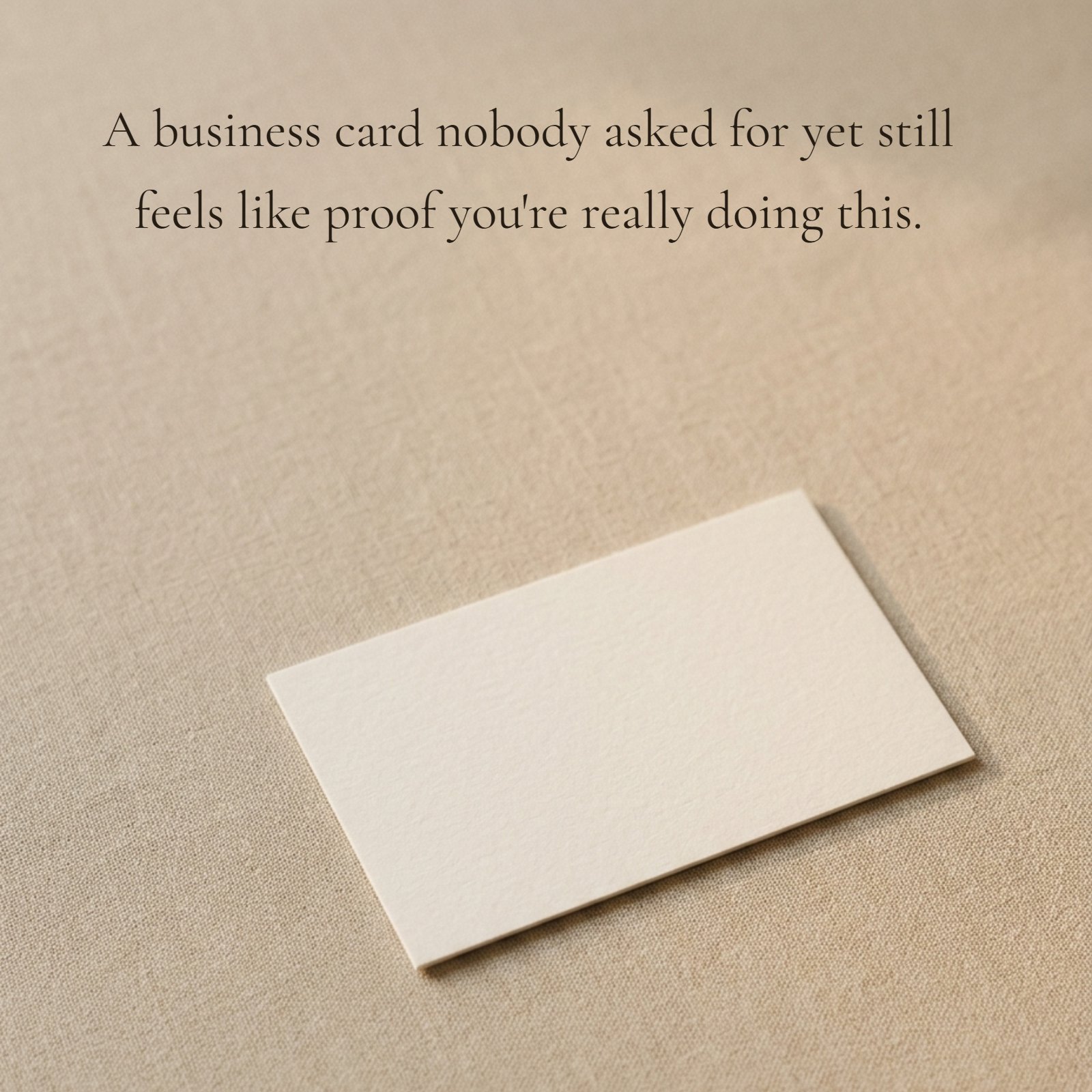 A high-resolution photo of a single, cream-colored blank business card centered on a light beige textured fabric surface with soft natural lighting and negative space.