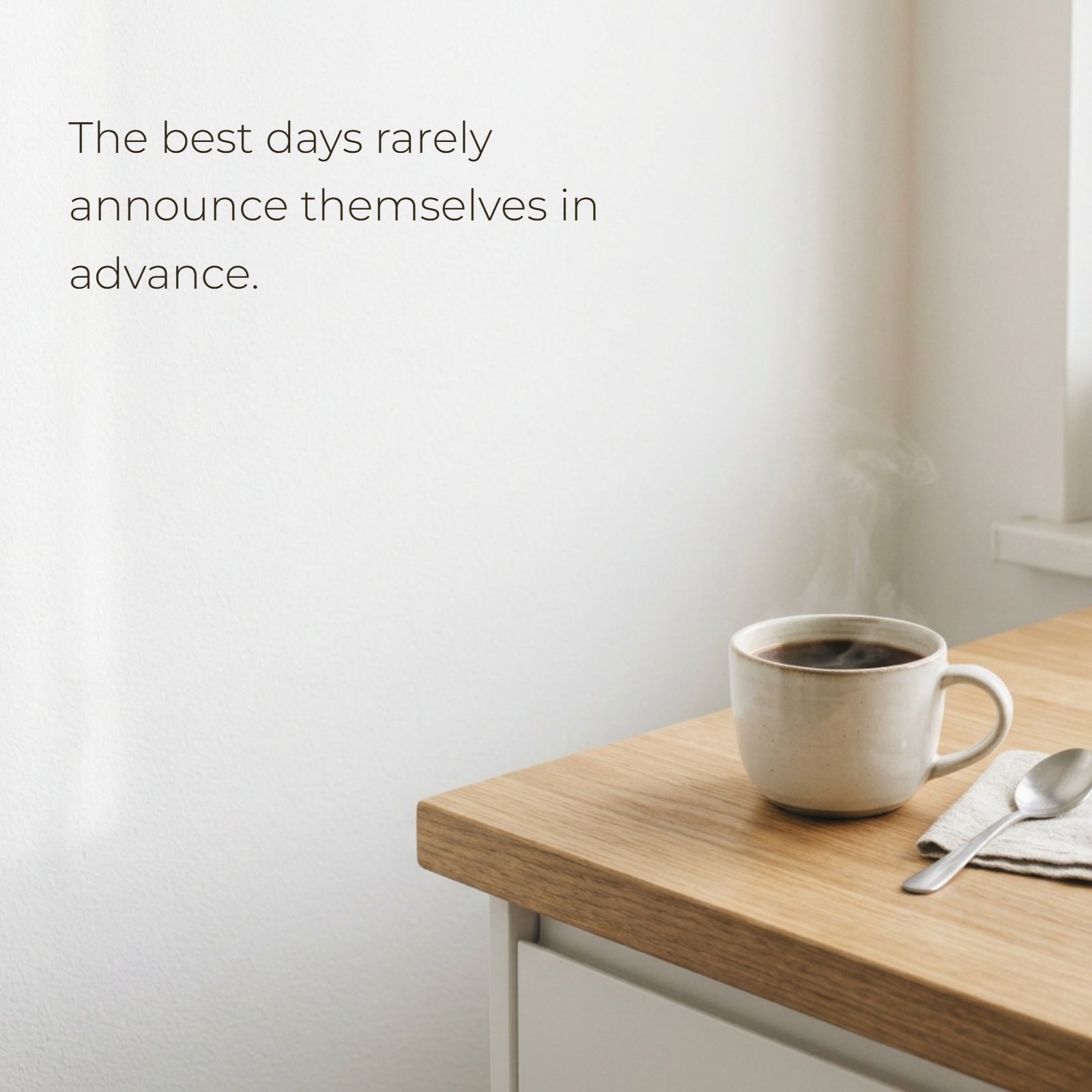 A minimalist morning photograph featuring a steaming cup of coffee on a wooden counter next to a large blank white wall containing the quote, 'The best days rarely announce themselves in advance.'