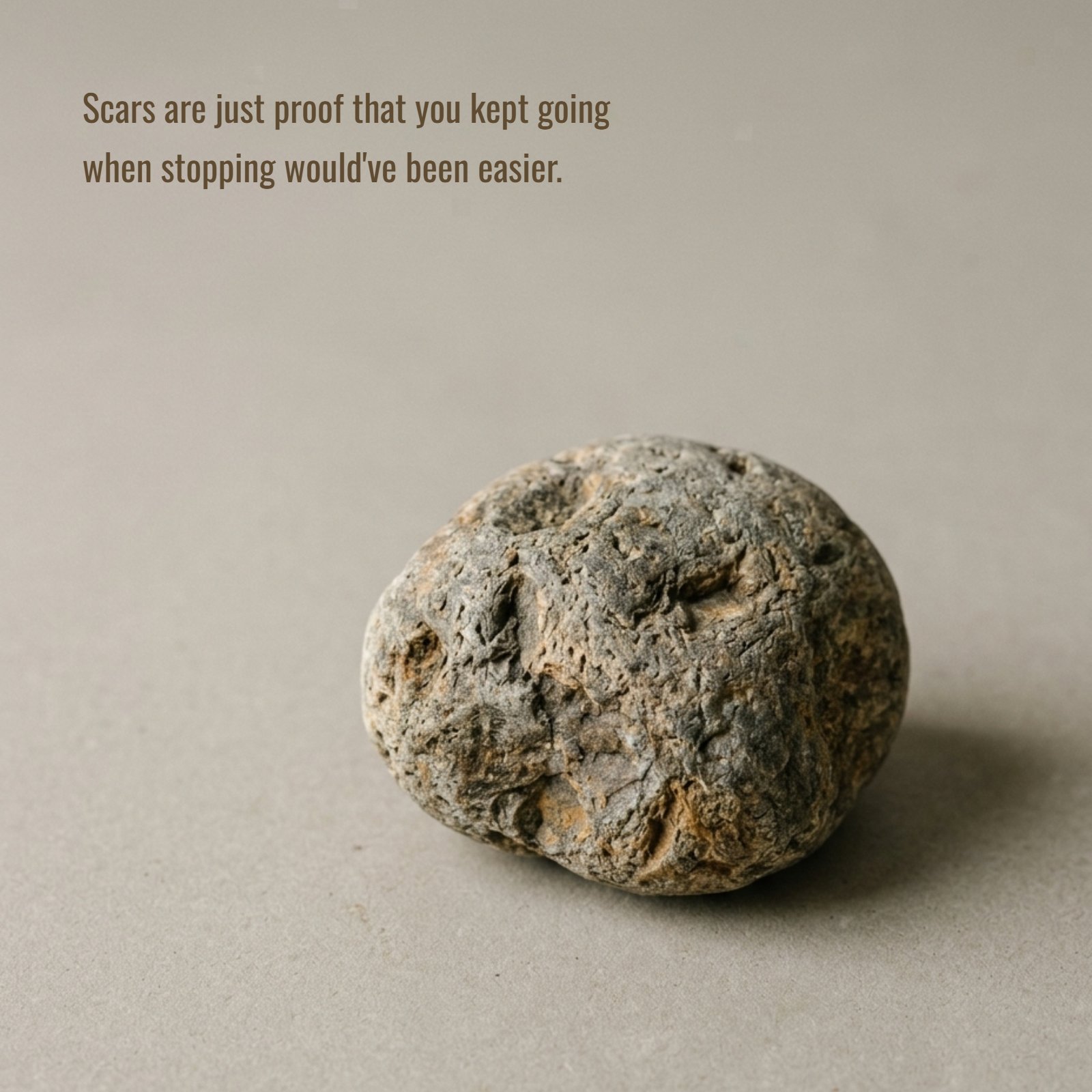 A minimalist photograph of a single weathered stone with texture on a plain neutral surface, featuring the courage quote: "Scars are just proof that you kept going when stopping would've been easier."