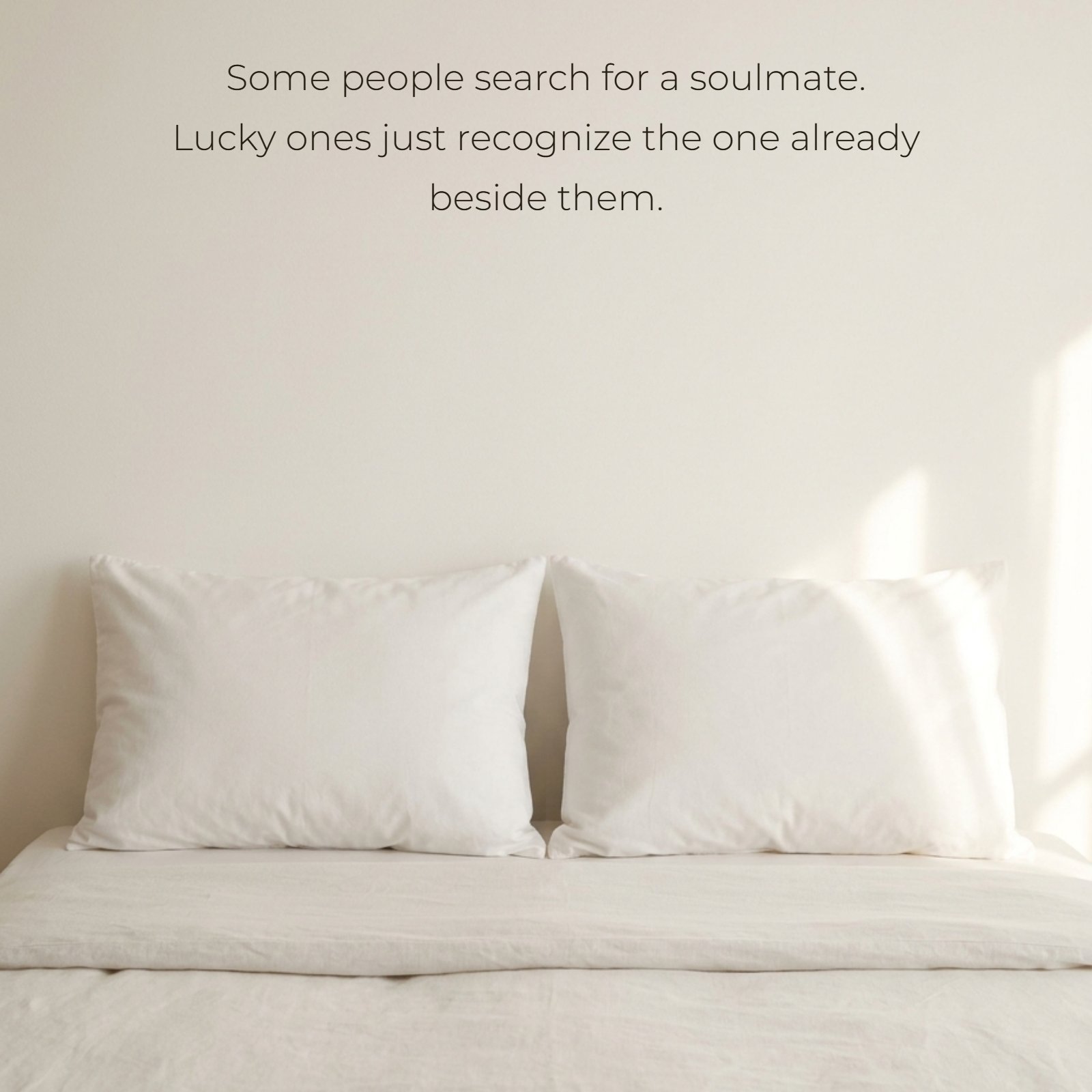 A minimalist photo showing two plain white pillows placed side-by-side on a neatly made bed with soft morning light. The image contains clean negative space for the quote: Some people search for a soulmate. Lucky ones just recognize the one already beside them.