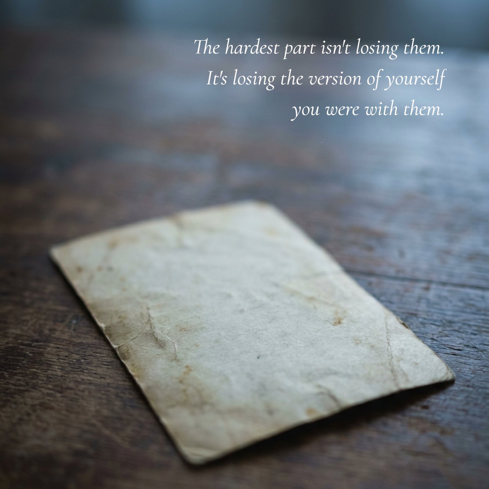 A minimalist, soft-focus photo of a faded, face-down photograph on a dark wooden table in blue-grey light. Overlaid is the text: The hardest part isn't losing them. It's losing the version of yourself you were with them.