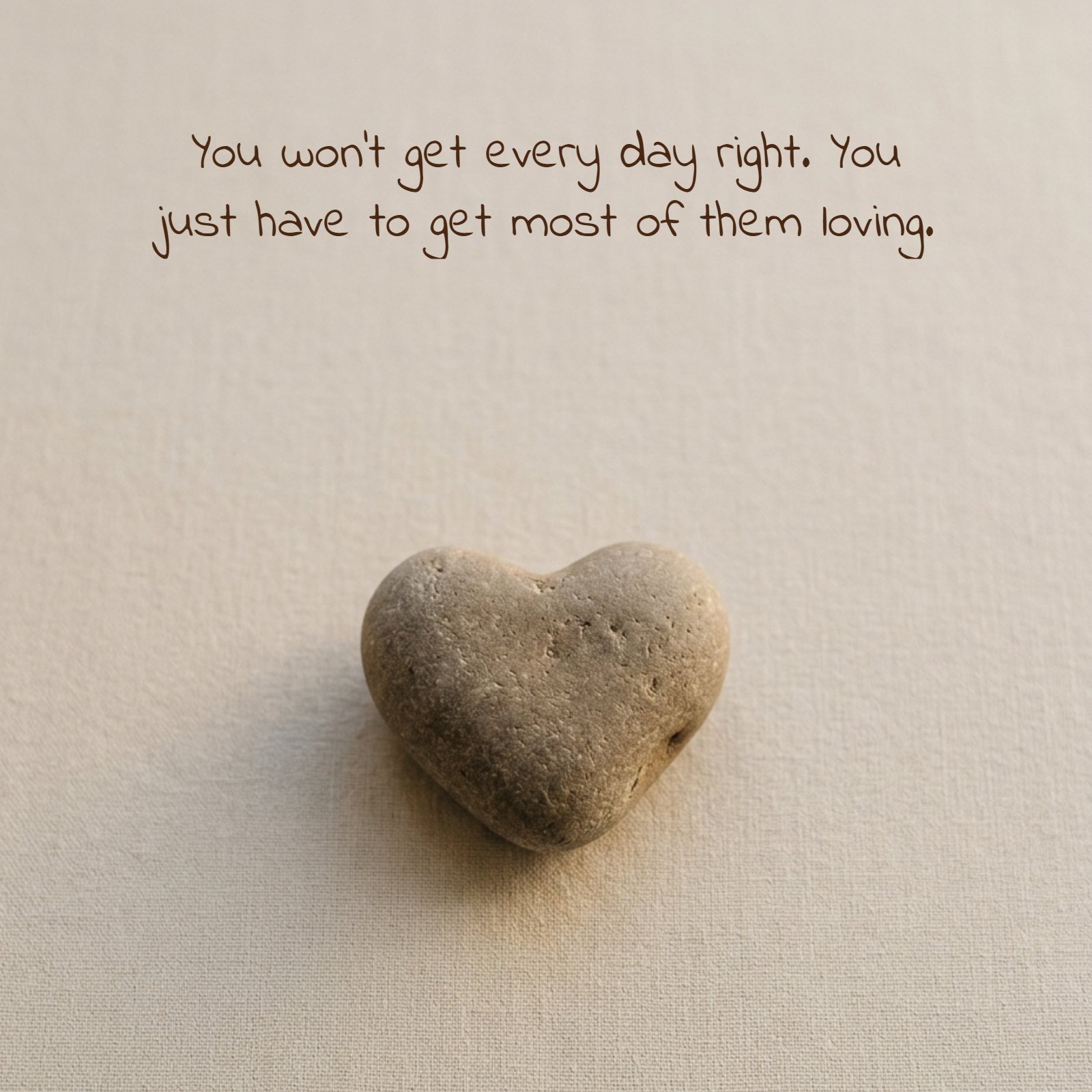 A minimalist photo of a small heart-shaped stone on a plain neutral surface with the text 'You won't get every day right. You just have to get most of them loving.' superimposed in a casual handwritten font.