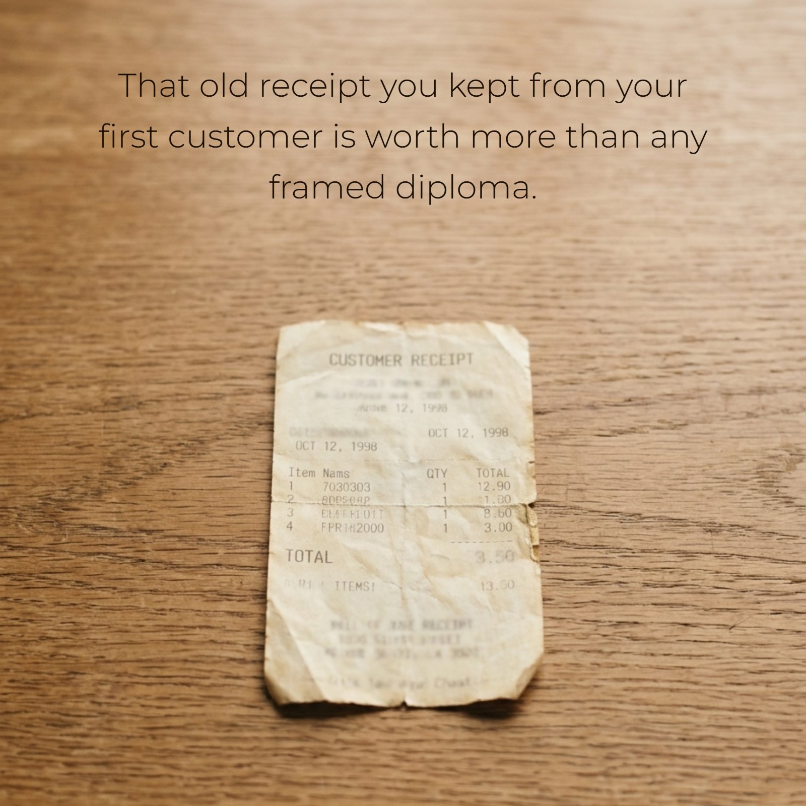 A minimalist photograph with plenty of negative space, showing a worn, yellowed customer receipt dated October 12, 1998, placed in the center of a wooden desk. Overlaid on the upper negative space is the text: That old receipt you kept from your first customer is worth more than any framed diploma.