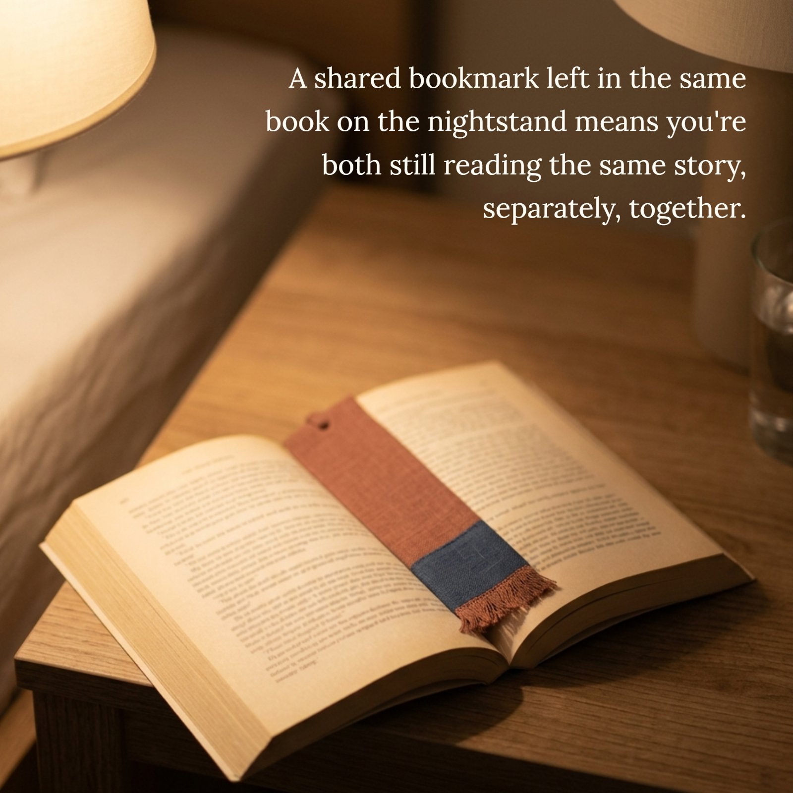 A minimalist photo of an open book with a simple bookmark resting on a wooden nightstand under soft warm light, with the quote 'A shared bookmark left in the same book on the nightstand means you're both still reading the same story, separately, together' written above it.