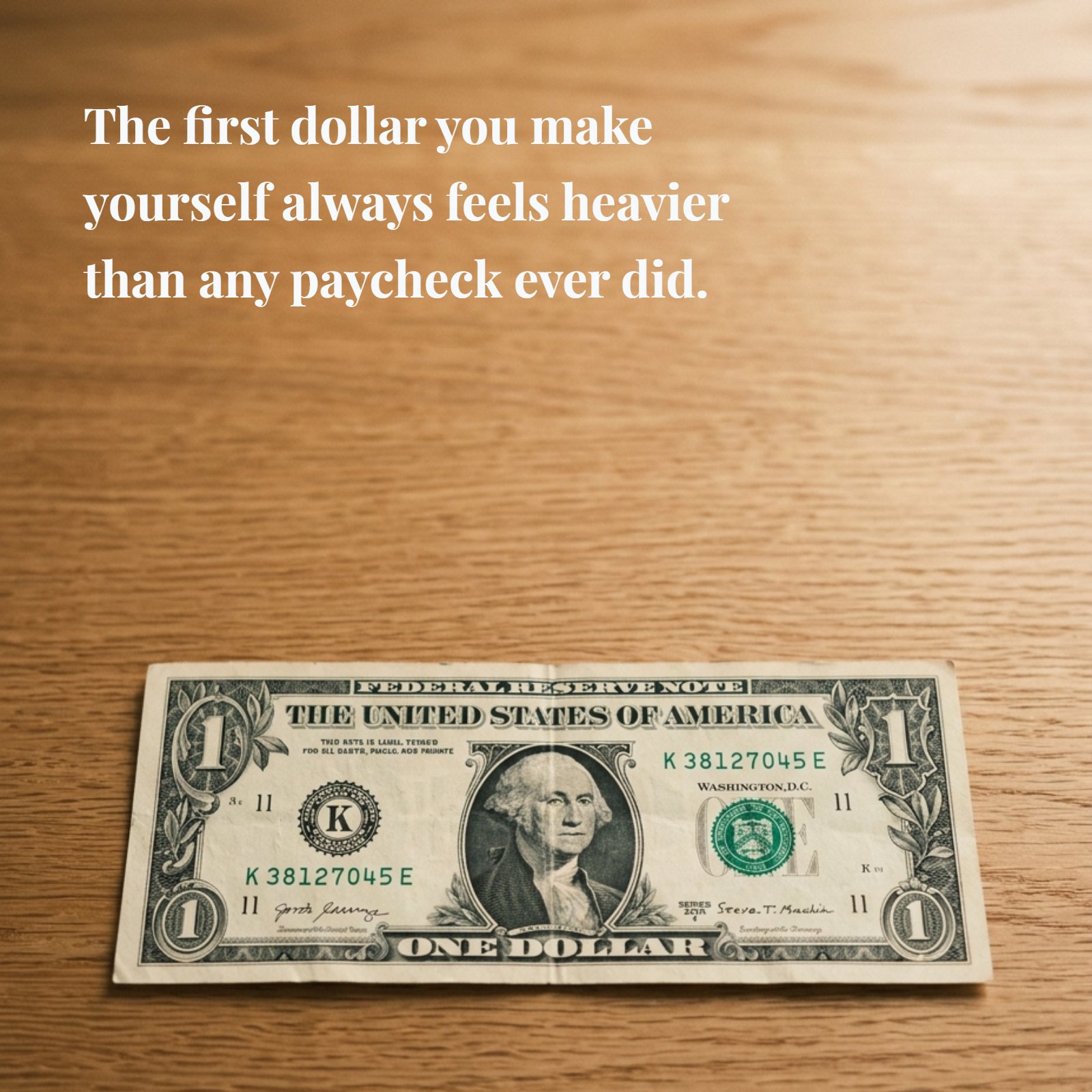 A 1:1 minimalist close-up photograph of a US one-dollar bill resting flat on a plain wooden desk under soft warm light. Overlaid on the upper negative space is the text: 'The first dollar you make yourself always feels heavier than any paycheck ever did.'