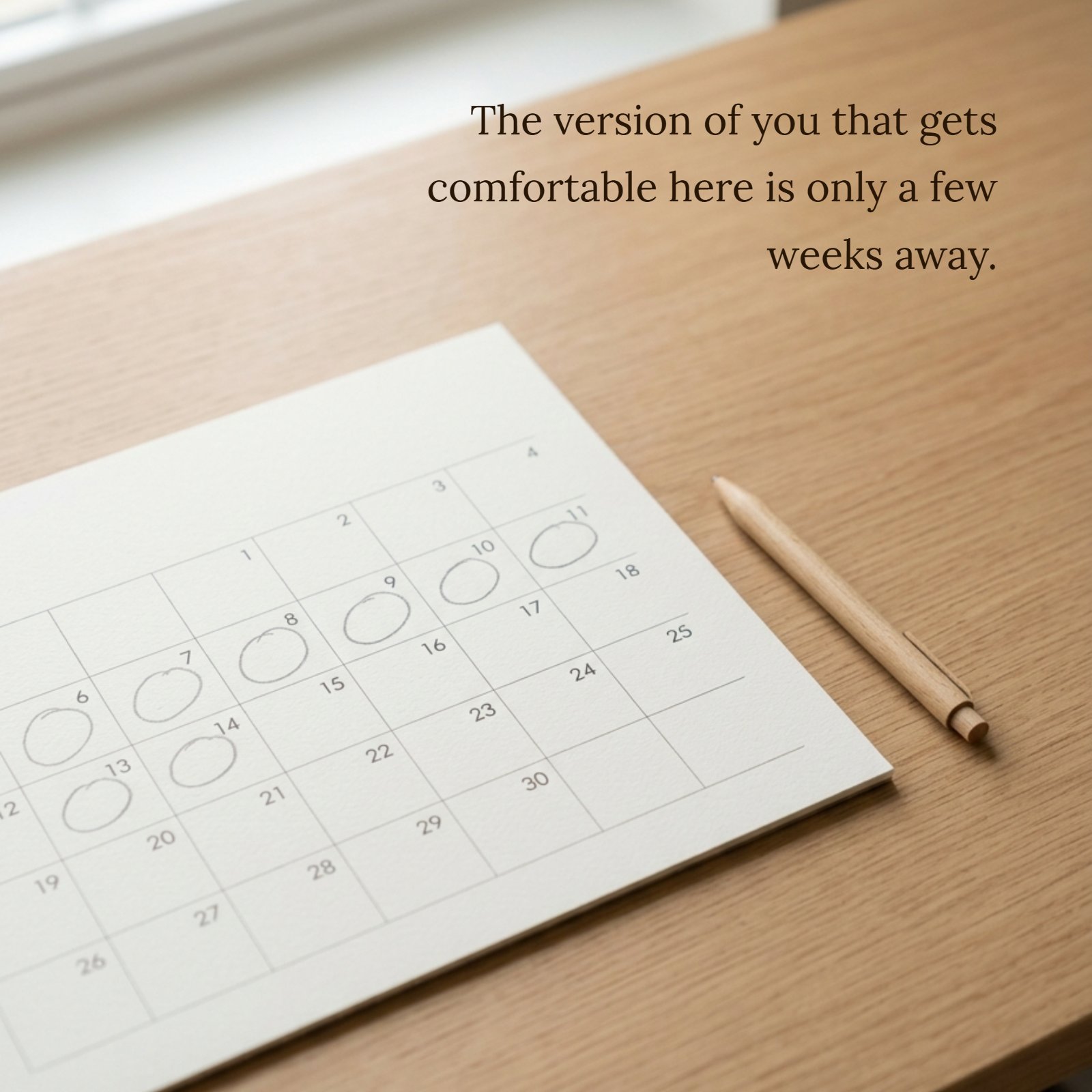 A minimalist photo of a single calendar page on a clean neutral desk with a pen, with the quote text "The version of you that gets comfortable here is only a few weeks away" overlaid on the negative space. Several future weeks are visibly marked.
