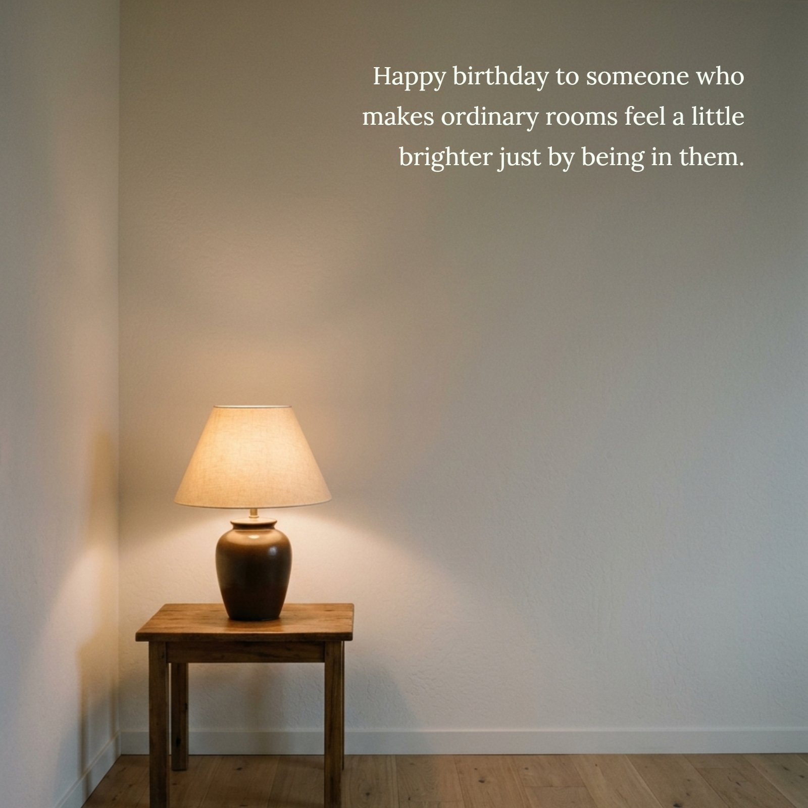 Minimalist photo of a glowing table lamp on a wooden table in a room corner, featuring the quote "Happy birthday to someone who makes ordinary rooms feel a little brighter just by being in them."