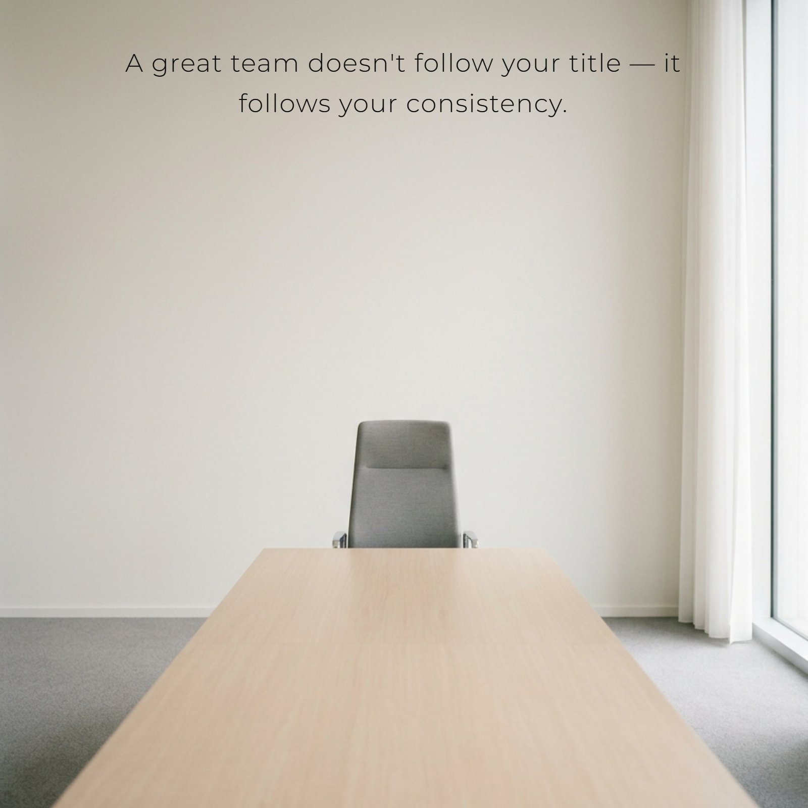 Minimalist vertical photo of a single grey ergonomic office chair at the head of a plain light wood conference table, bathed in soft daylight. The text overlay reads, “A great team doesn't follow your title — it follows your consistency.”