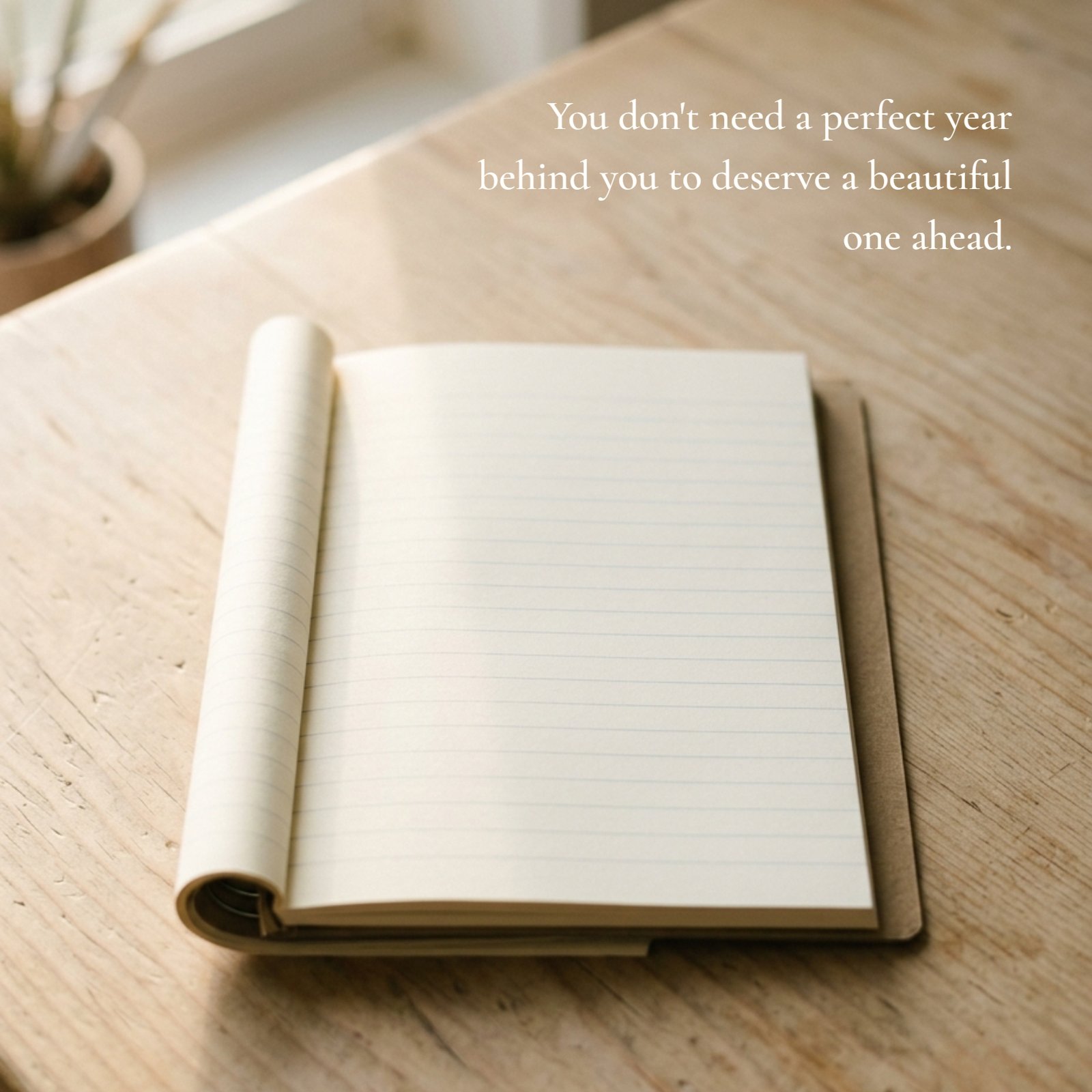 Minimalist photo of a blank lined notebook page on a wooden desk with a pot plant near a window in soft morning light, featuring the inspirational quote: 'You don't need a perfect year behind you to deserve a beautiful one ahead.'