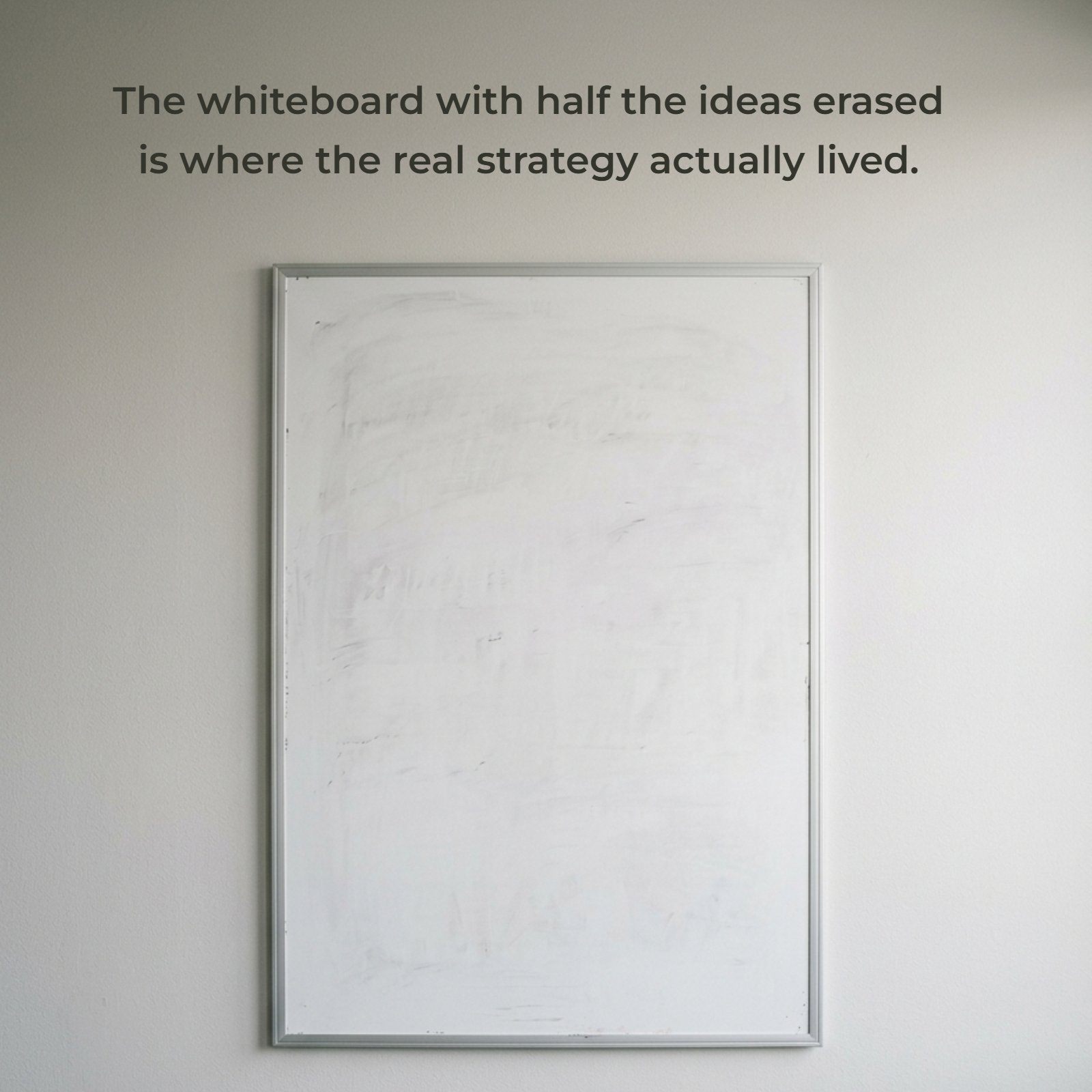 A minimalist vertical photo of a single used whiteboard on a plain office wall with the quote "The whiteboard with half the ideas erased is where the real strategy actually lived." clearly written on it.