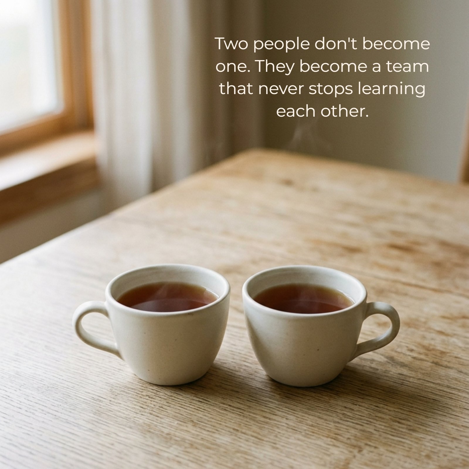 Minimalist 1:1 image of two plain steaming tea cups side-by-side on a light wood table, featuring the quote "Two people don't become one. They become a team that never stops learning each other." in simple font.
