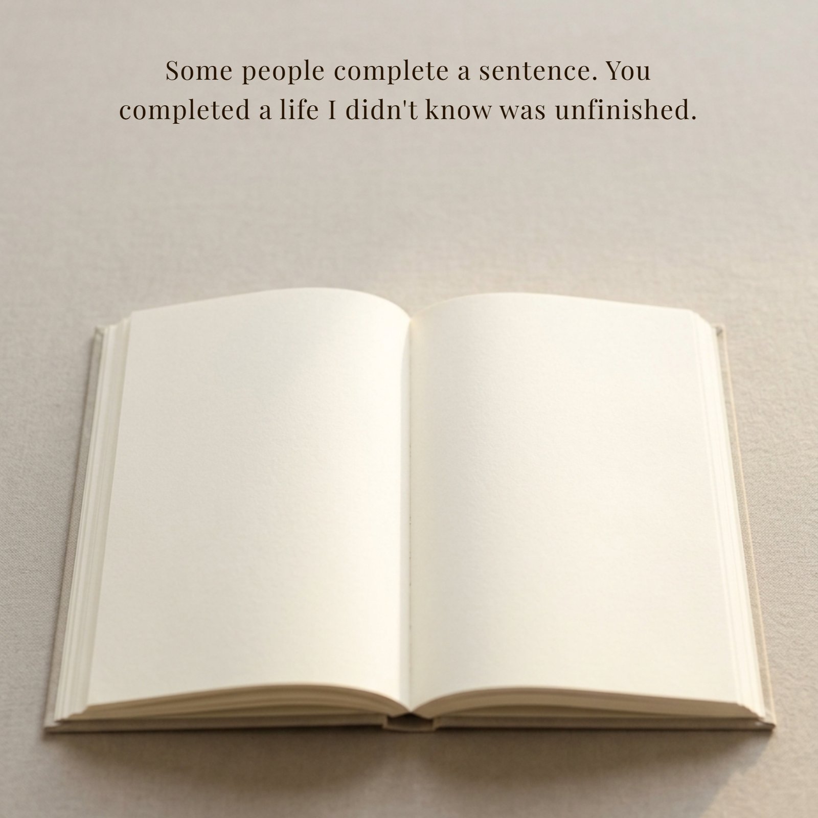 Minimalist 1:1 photograph of an open blank book with creamy pages, centered on a plain neutral textured surface. Overlaid in elegant, dark serif text across the open pages is the quote, "Some people complete a sentence. You completed a life I didn't know was unfinished." Soft warm light illuminates the scene, which has clean negative space.