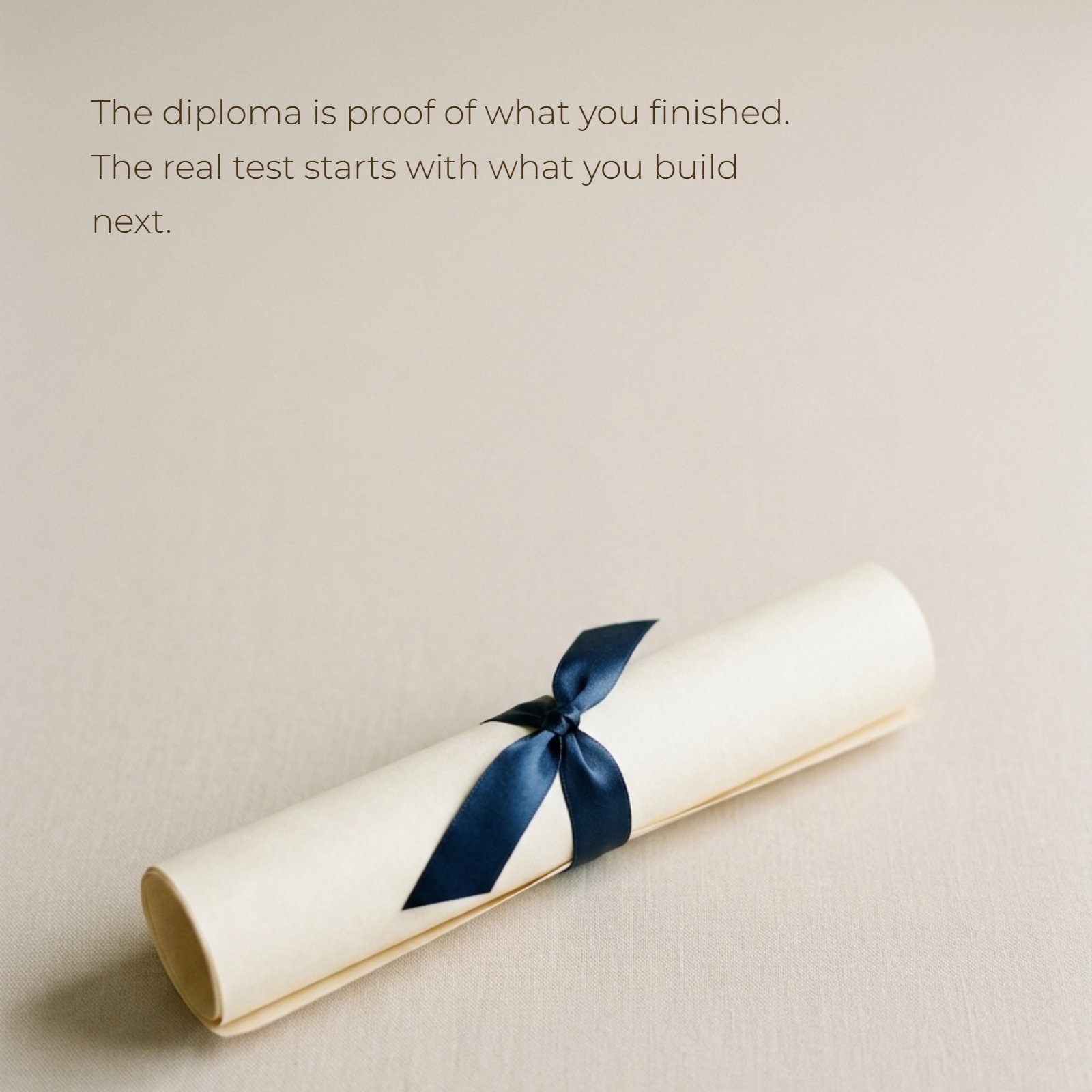 A minimalist photo of a single rolled diploma tied with a blue ribbon, featuring the overlay text: The diploma is proof of what you finished. The real test starts with what you build next.