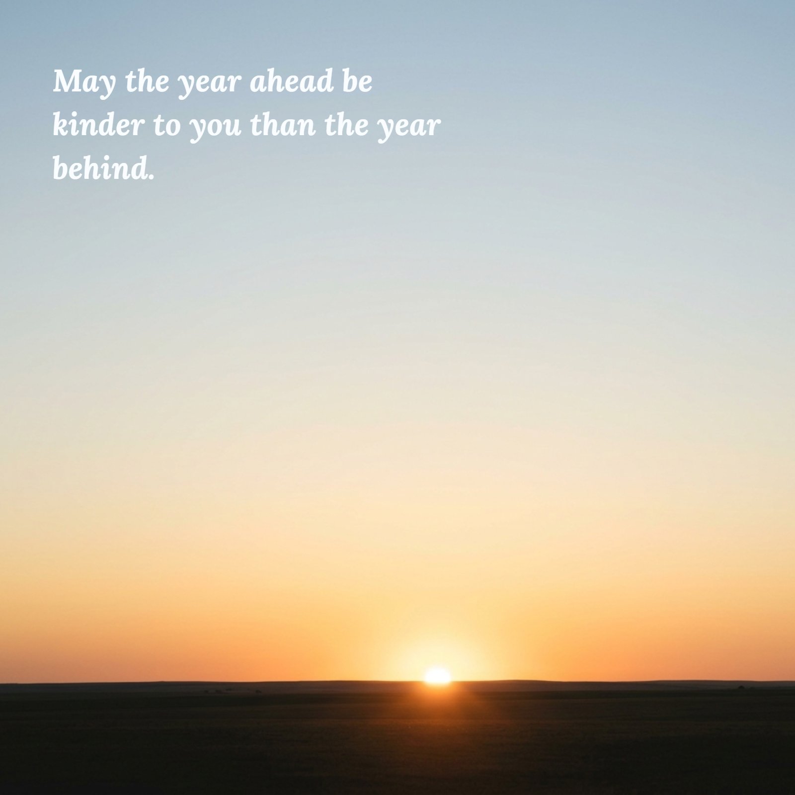 A minimalist photo of a plain horizon during sunrise, with soft, warm golden light breaking. Centered in the gradient sky, the quote text "May the year ahead be kinder to you than the year behind" is written in an elegant, bold serif font, colored in a soft warm grey to complement the sky.