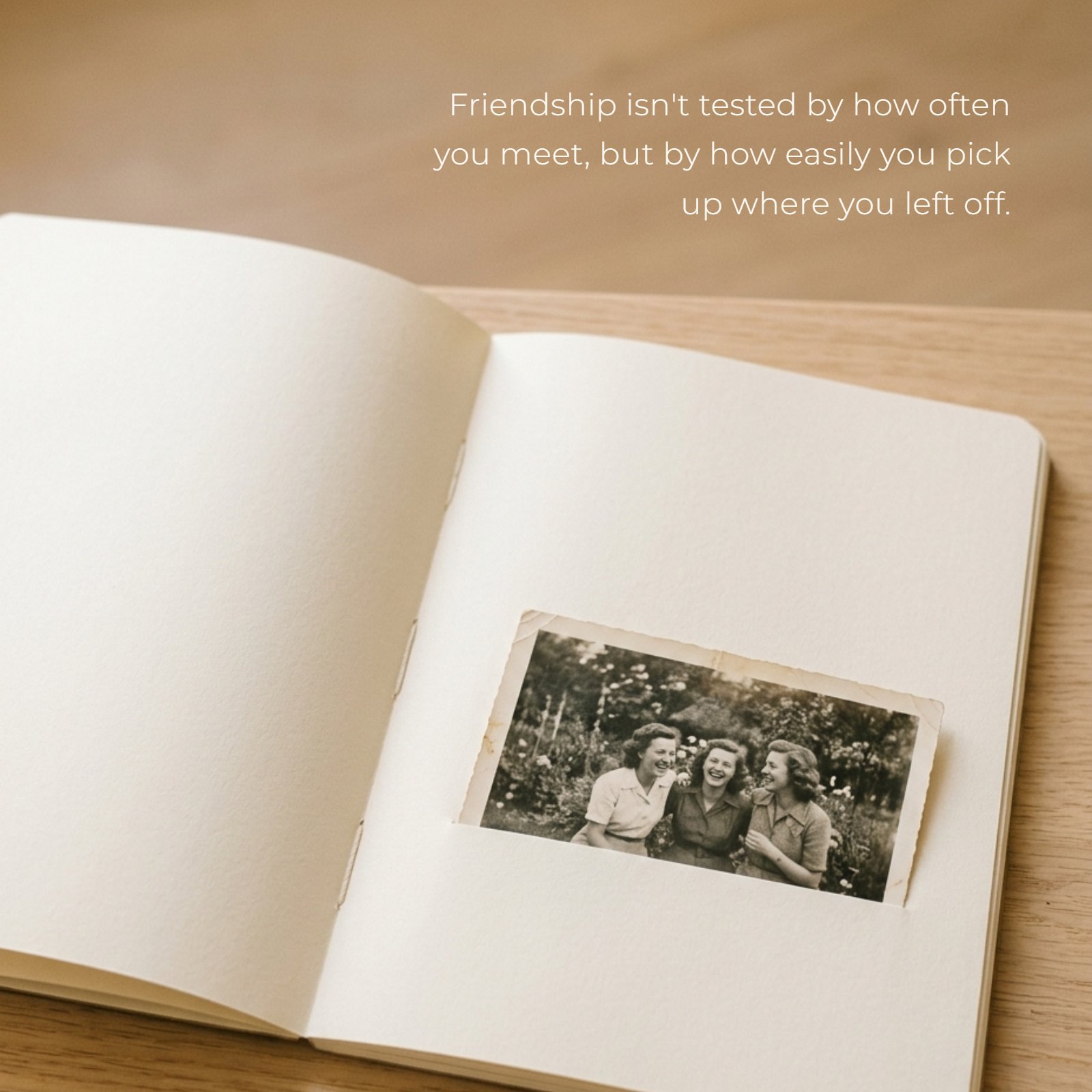 Minimalist 1:1 photo of a vintage black and white picture of three friends, slightly faded, tucked into the blank cream page of an open journal, with the handwritten text overlay 'Friendship isn't tested by how often you meet, but by how easily you pick up where you left off.' The image is lit by soft, warm light with ample clean negative space.