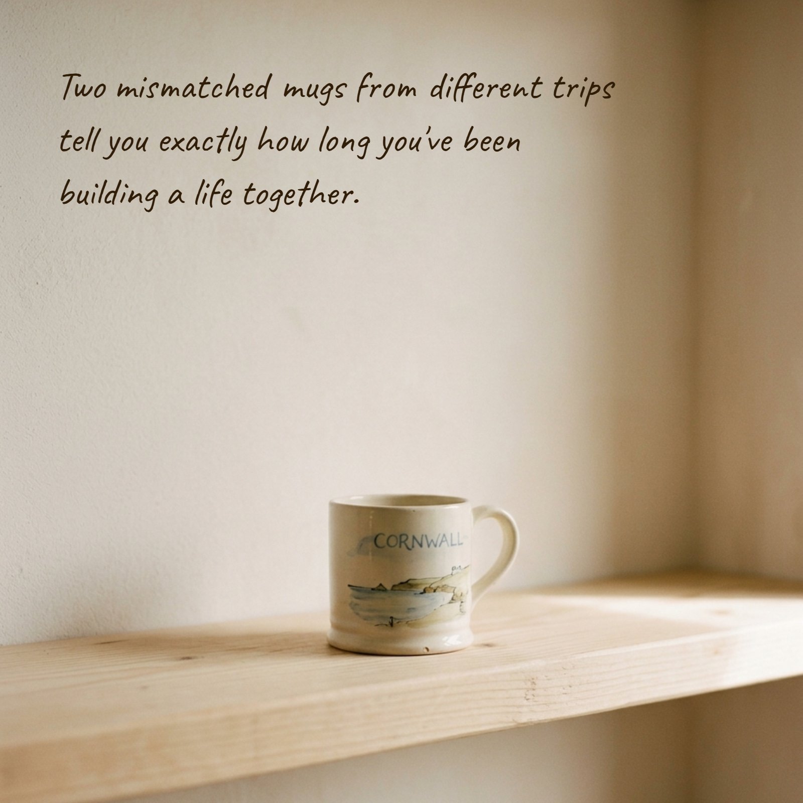 A minimalist photo showing a single souvenir mug from Cornwall on a simple wooden shelf with soft light. The space above is clear for adding text, like the quote: "Two mismatched mugs from different trips tell you exactly how long you've been building a life together."