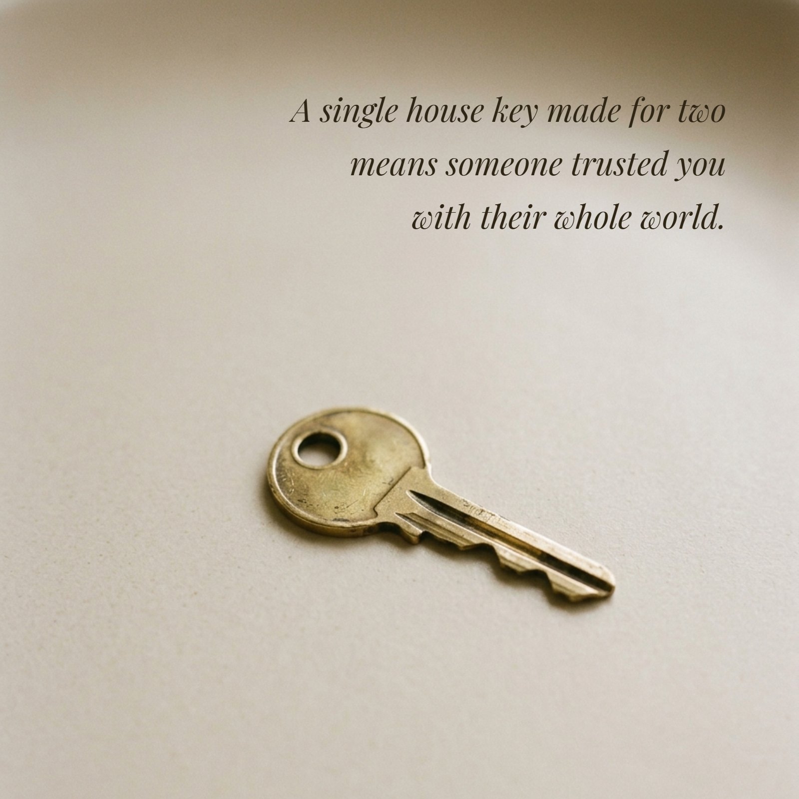 A minimalist 1:1 photograph shows a single brass house key lying on a plain neutral surface under soft warm light. Overlaid on the image in italic text is the quote: "A single house key made for two means someone trusted you with their whole world."