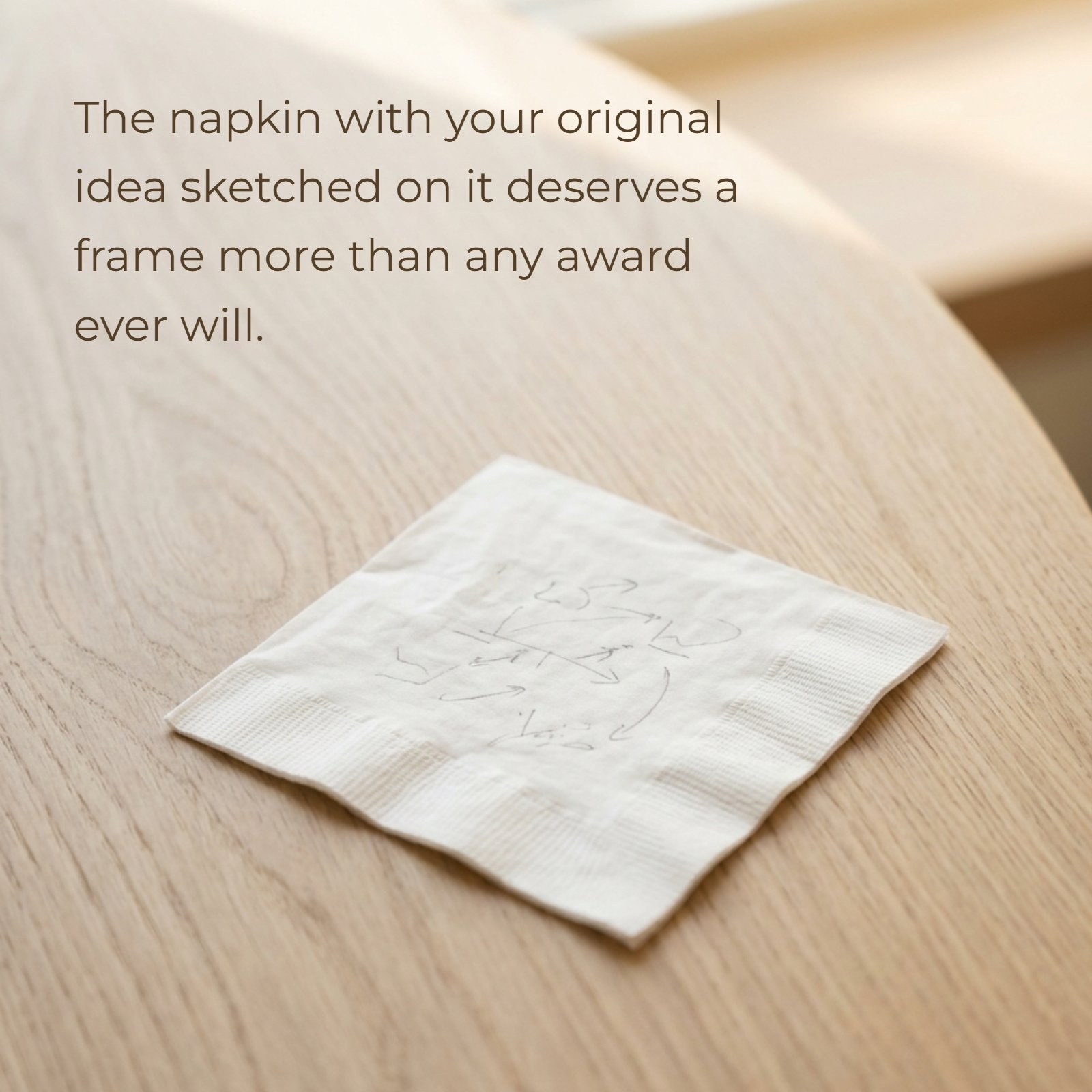 A minimalist vertical photograph of a crumpled white napkin with faint pencil sketch marks, resting centrally on a plain light wood café table under soft light. The napkin represents the core idea in the entrepreneurial quote: The napkin with your original idea sketched on it deserves a frame more than any award ever will.