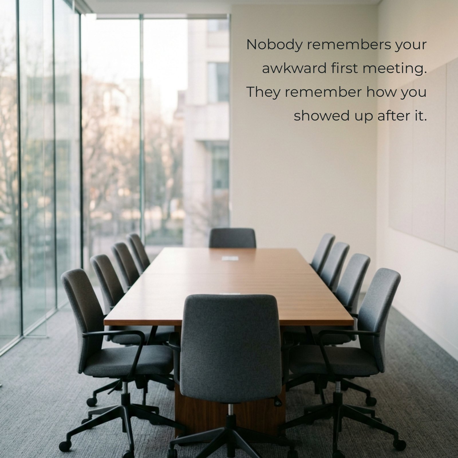 A minimalist photo of a single wooden conference table with empty grey office chairs. Over the top wall, the motivational quote “Nobody remembers your awkward first meeting. They remember how you showed up after it” is written in a clean white sans-serif font.