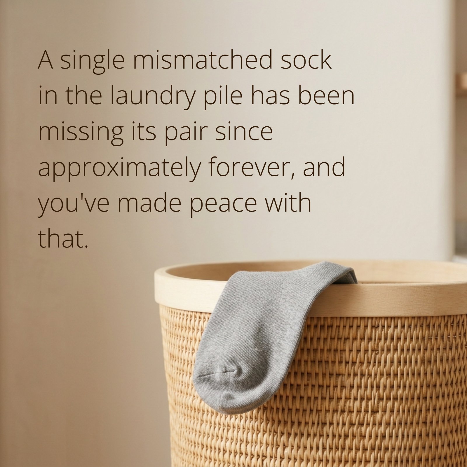 Minimalist 1:1 photograph featuring a single textured knit sock resting on the edge of a plain laundry basket against a soft, light background, including the text overlay: 'A single mismatched sock in the laundry pile has been missing its pair since approximately forever, and you've made peace with that.'