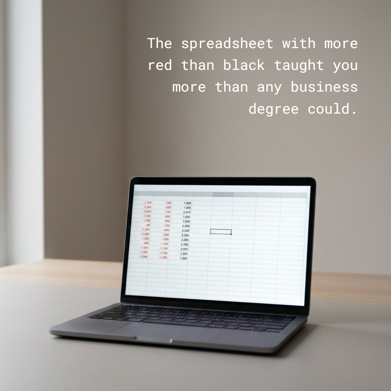 Minimalist 1:1 photograph featuring a single laptop on a neutral desk in soft light. The screen displays a clear spreadsheet with prominent red negative figures among a few black ones. Blank wall space above is ideal for the text: The spreadsheet with more red than black taught you more than any business degree could.
