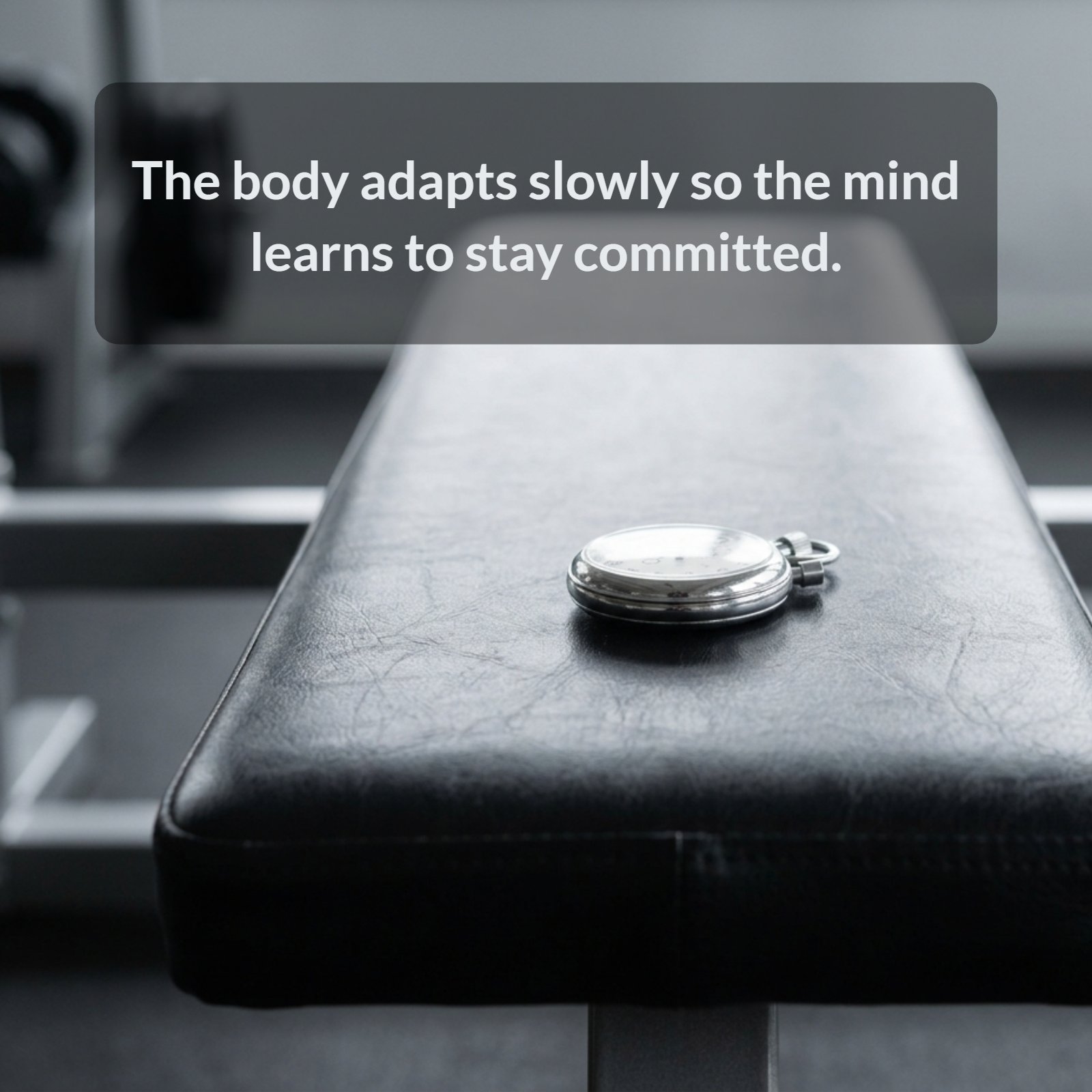 A minimalist photograph of a single mechanical stopwatch resting on a black gym bench, symbolizing the time and dedication required for physical adaptation and mental commitment in training.