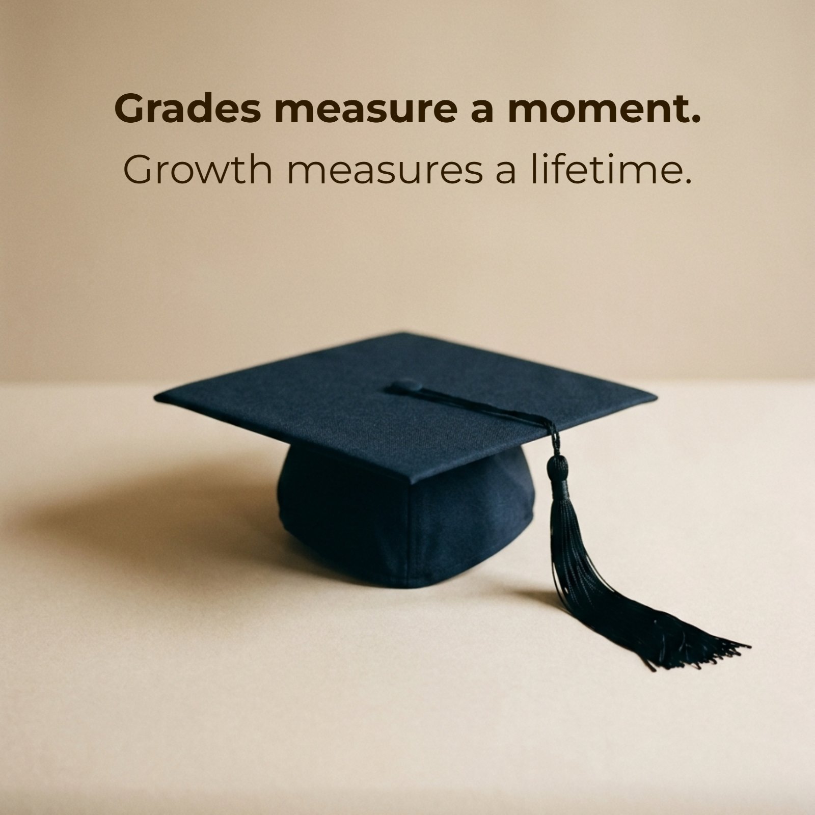 A minimalist photograph of a single black academic graduation cap resting on a plain, warm beige surface, featuring the overlay text: 'Grades measure a moment. Growth measures a lifetime.'