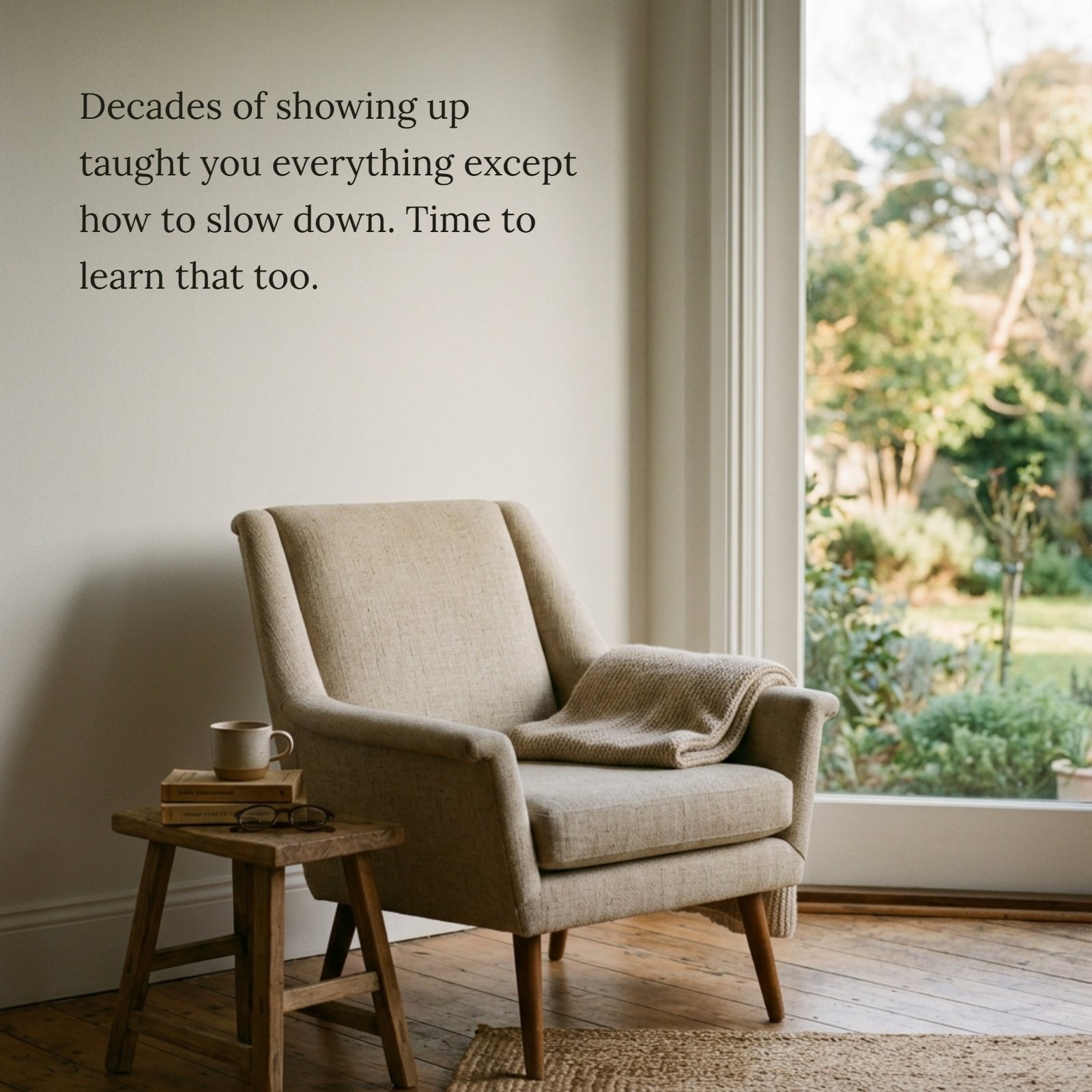 Minimalist scene with a beige armchair, blanket, and side table next to a large window overlooking a garden, featuring the text overlay 'Decades of showing up taught you everything except how to slow down. Time to learn that too.'