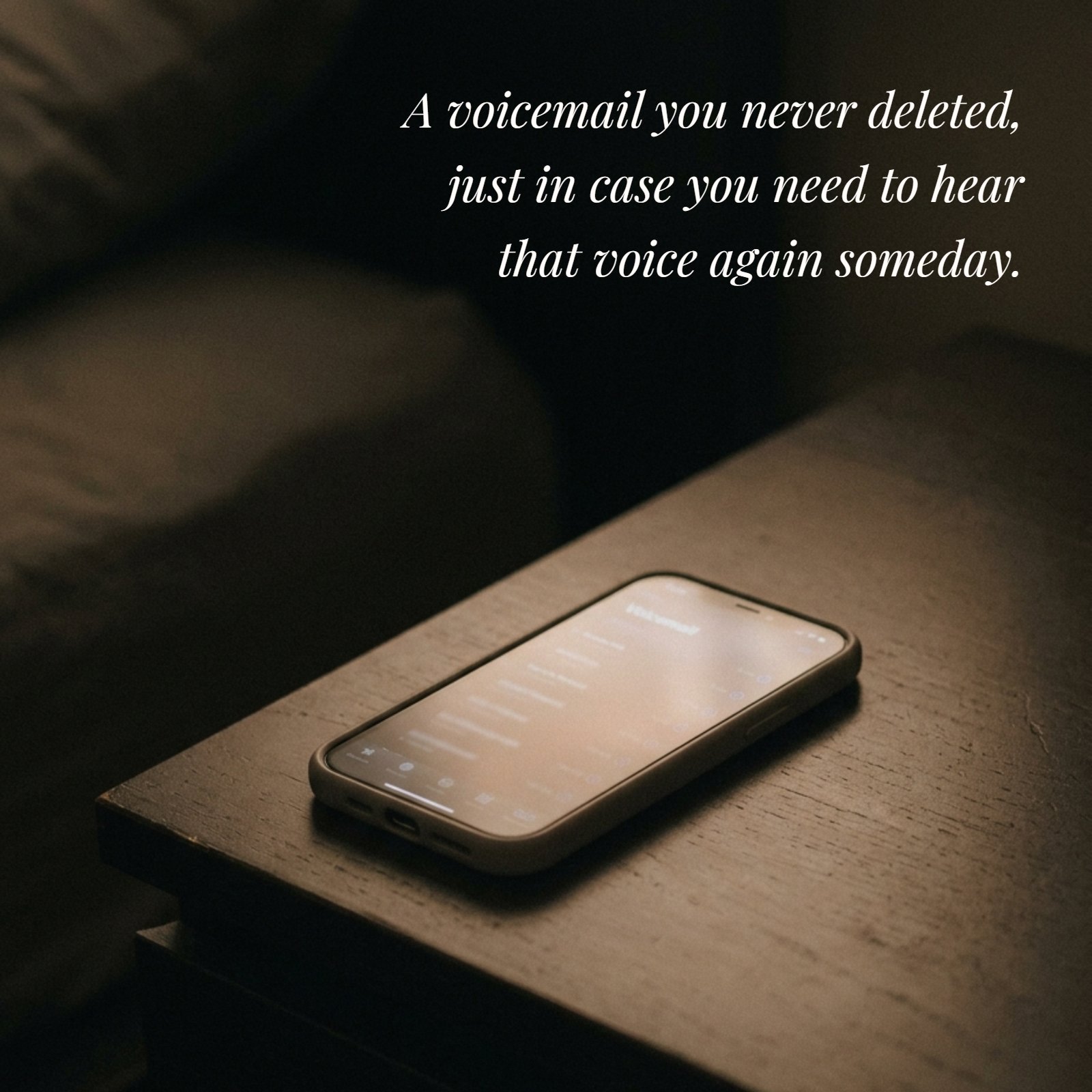 Minimalist 4:5 photograph showing a single phone screen glowing softly on a plain dark nightstand in muted warm light, featuring the text overlay 'A voicemail you never deleted, just in case you need to hear that voice again someday.'